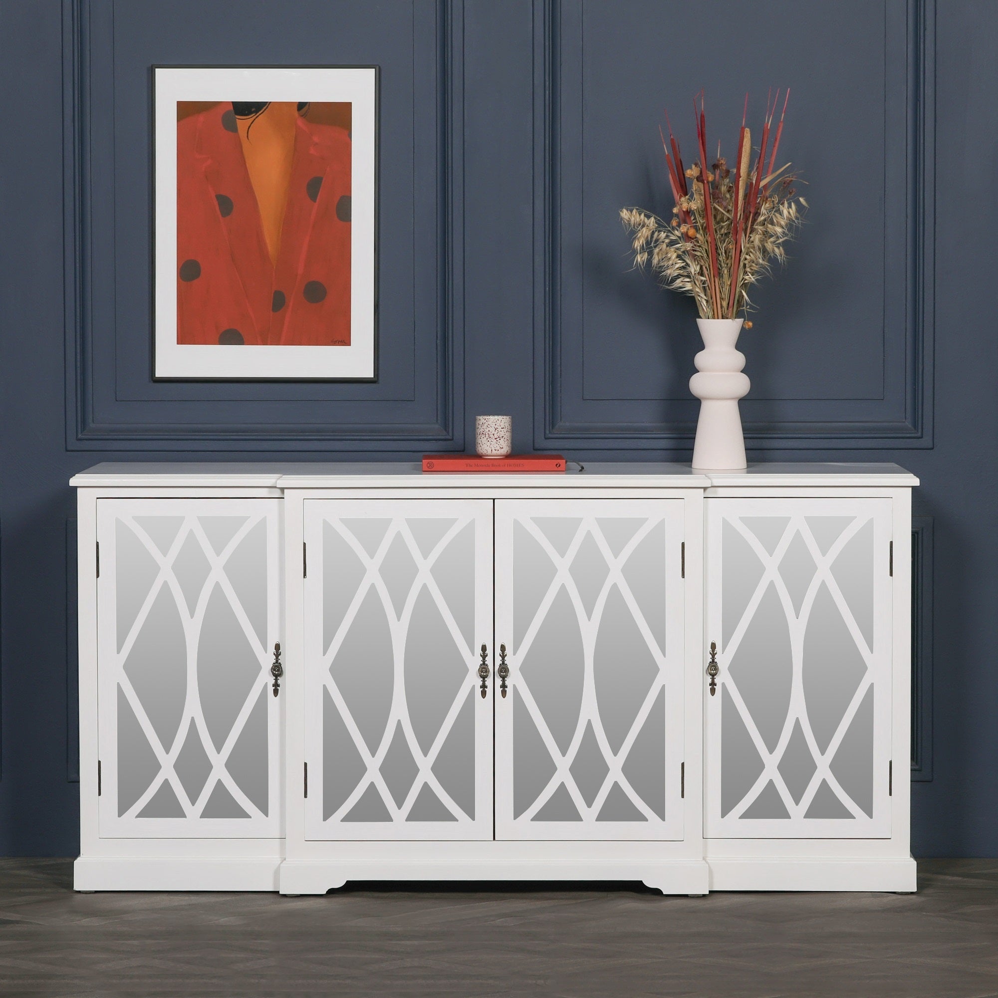 Anaïs White Mirrored Four Door Breakfront Sideboard styled against a navy panelled wall with decorative artwork and vase, featuring mirrored lattice glass doors, elegant white finish and spacious storage for luxury living and dining rooms.