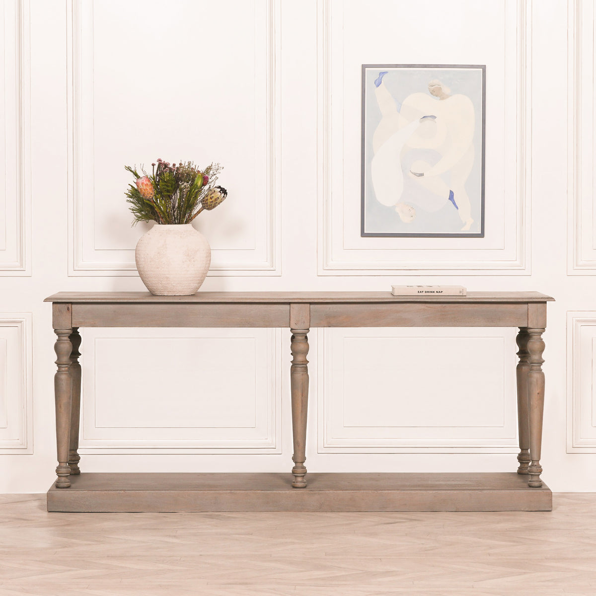Camille rustic wooden console table with six column legs styled in a contemporary hallway with decorative vase, floral arrangement and wall art, showcasing its versatility as a luxury hallway, living room or entrance console table.