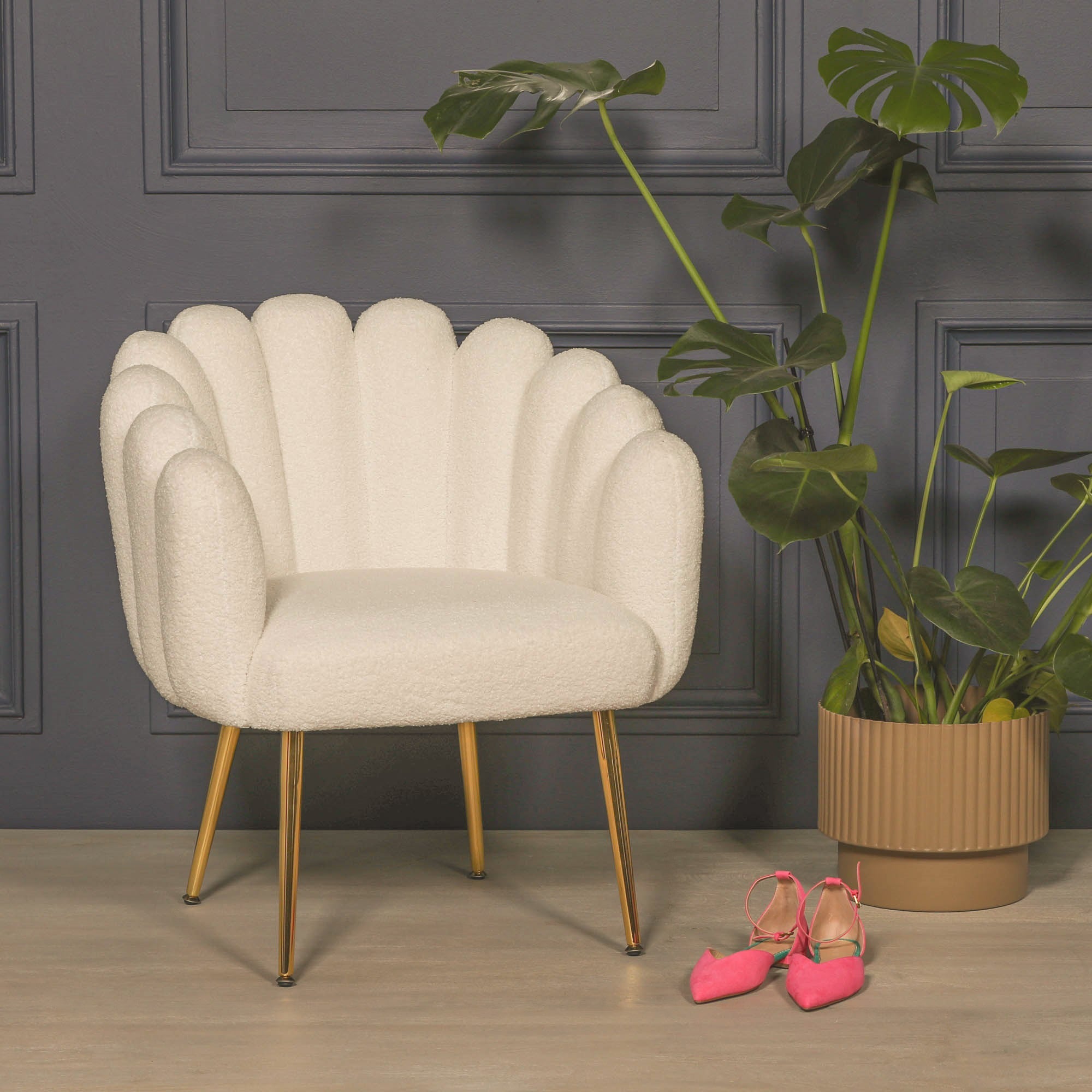 Elara Scalloped White Bouclé Dining Chair with Gold Metal Legs styled in a contemporary interior beside a large indoor plant, showcasing its sculptural scalloped backrest, textured bouclé upholstery and elegant gold metal legs.