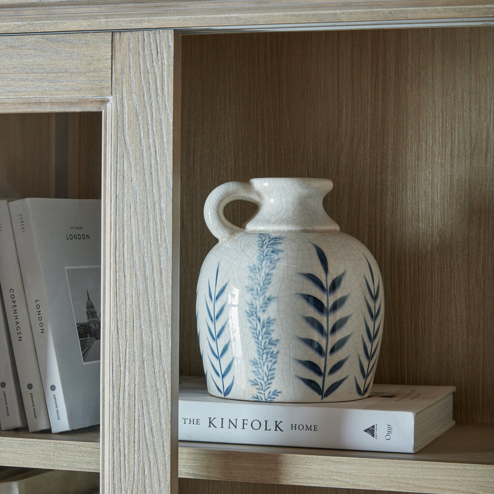 Decorative ceramic vase displayed on the Laurent Sliding Glass Dresser Cabinet Top with natural wood shelving, styled books and open display storage behind sliding glass doors.
