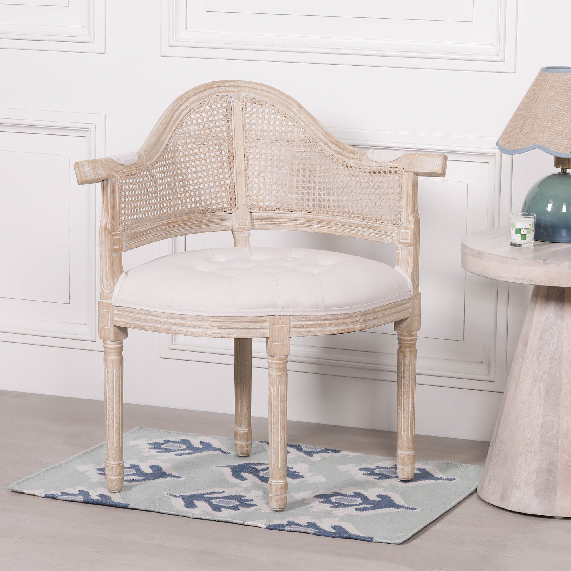 Lucienne Louis corner chair with linen upholstery, hand-woven cane backrest and washed wood frame styled in an elegant living room beside a side table and lamp.
