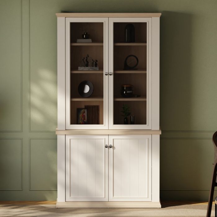 Montclair tall white and oak effect glazed display cabinet styled against a green panelled living room wall, with decorative objects displayed across the wooden shelves.