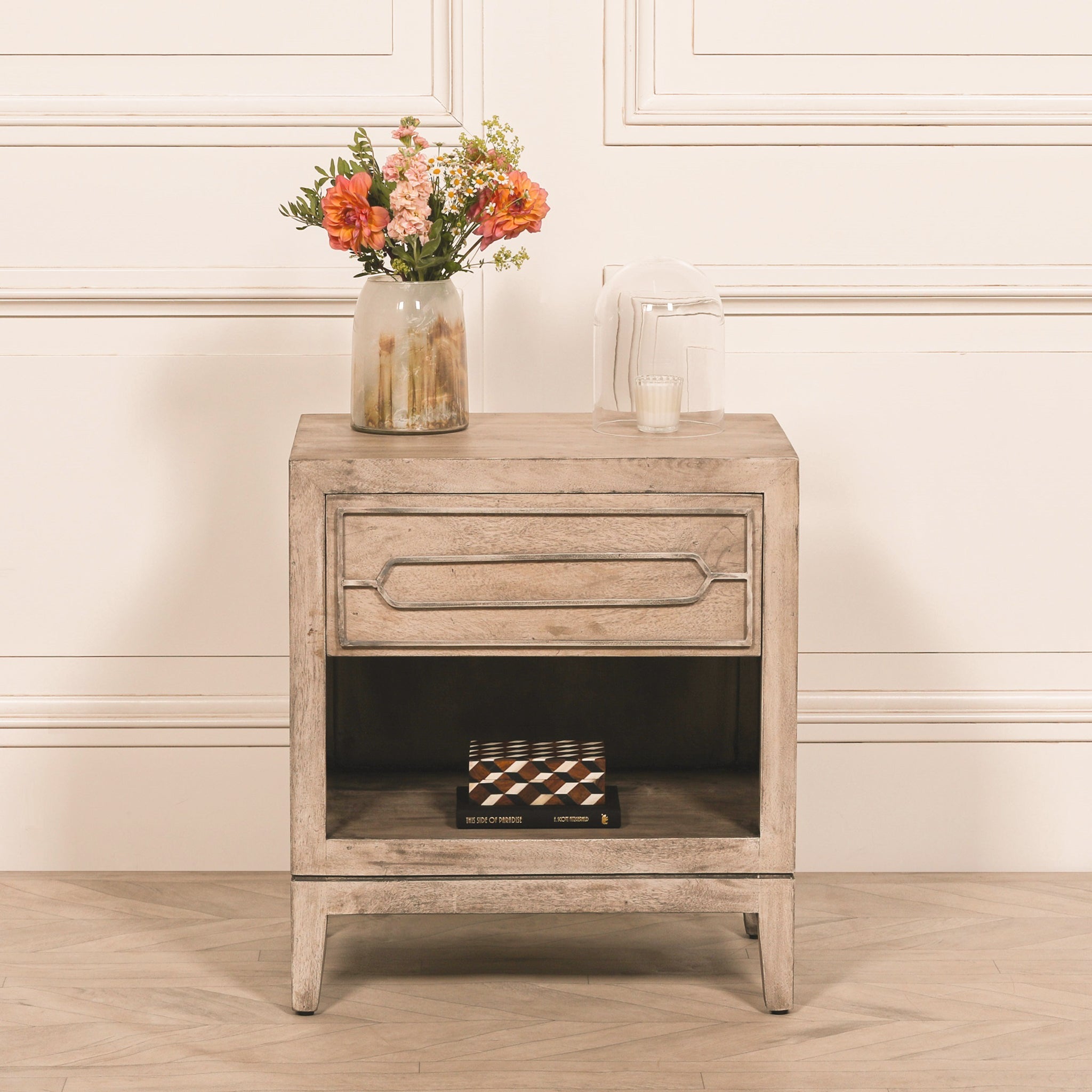 Soline rustic mango wood bedside table with drawer and lower shelf styled with a ceramic vase of flowers, decorative candle and books, showcasing its natural wood grain, spacious storage shelf and timeless bedroom furniture design.