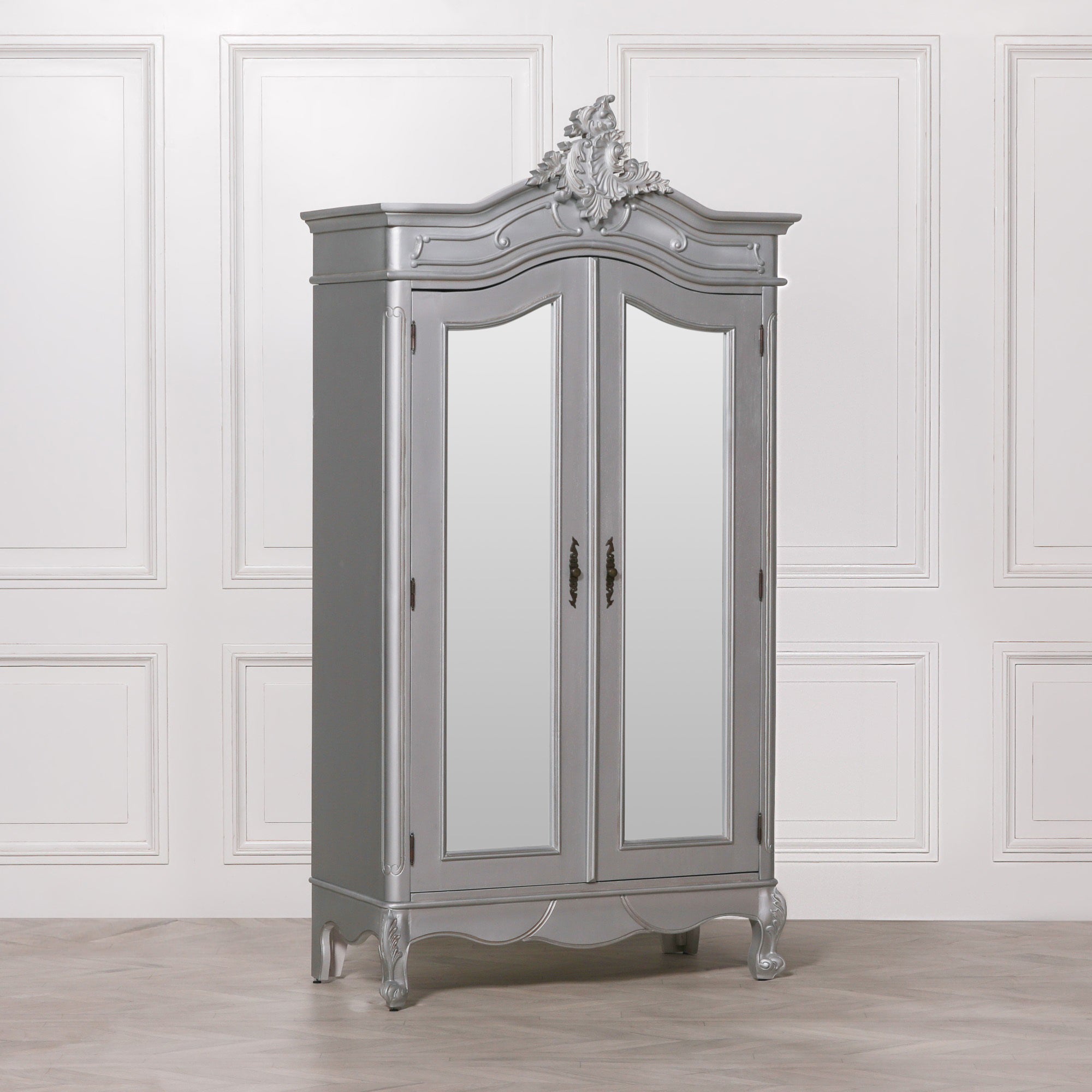 Vivienne Silver Carved Mirrored Double Door Armoire Wardrobe featuring elegant French Rococo styling, full-length mirrored doors, ornate hand-carved crown detailing, decorative cabriole feet and a luxurious silver finish, displayed in a sophisticated bedroom interior.