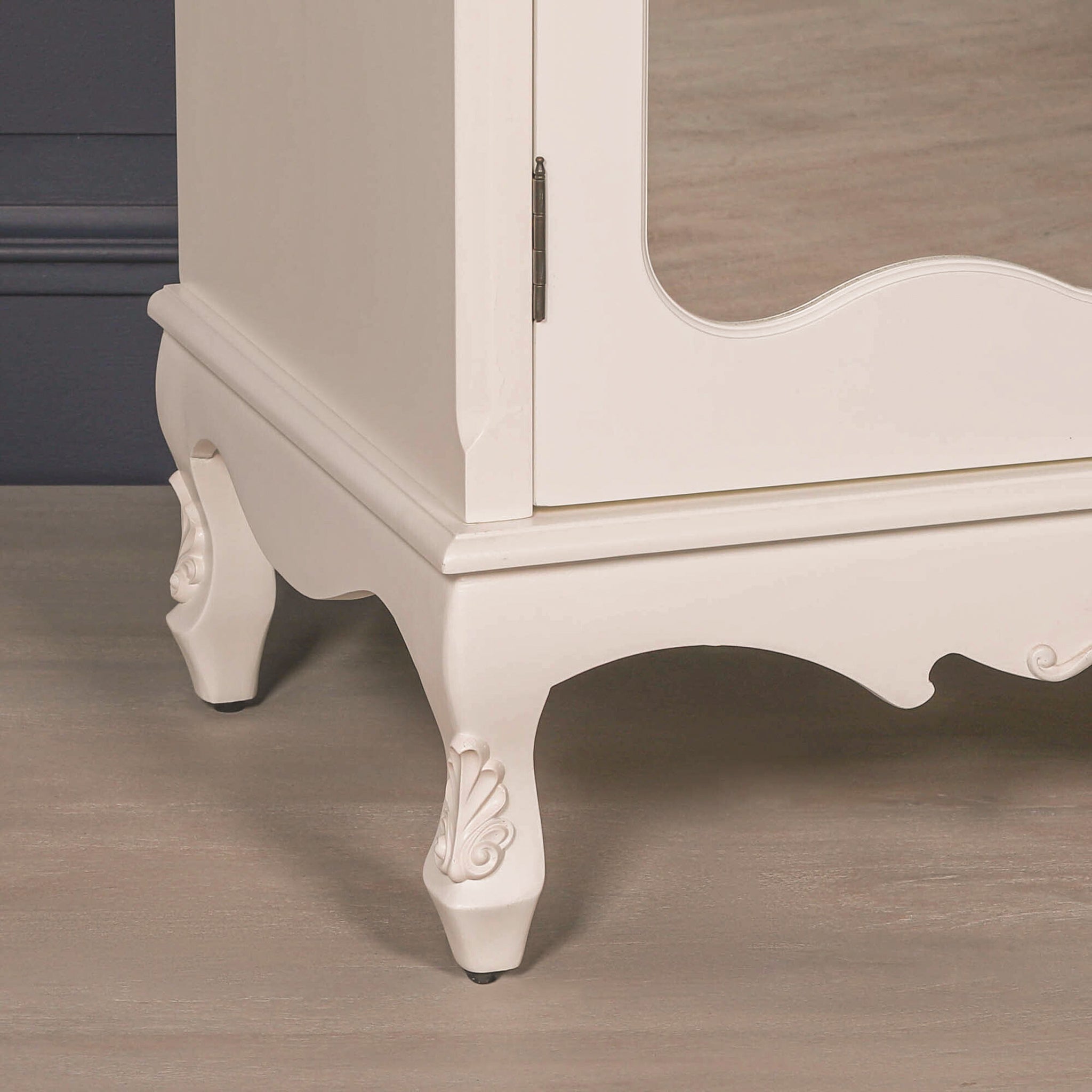 Carved leg and base detail of white mirrored armoire wardrobe with decorative finish