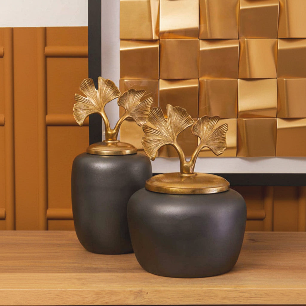 Alix grey and gold ginkgo leaf decorative ginger jars styled together on a wooden console, showing their rounded dark aluminium bodies and sculptural gold botanical lids.