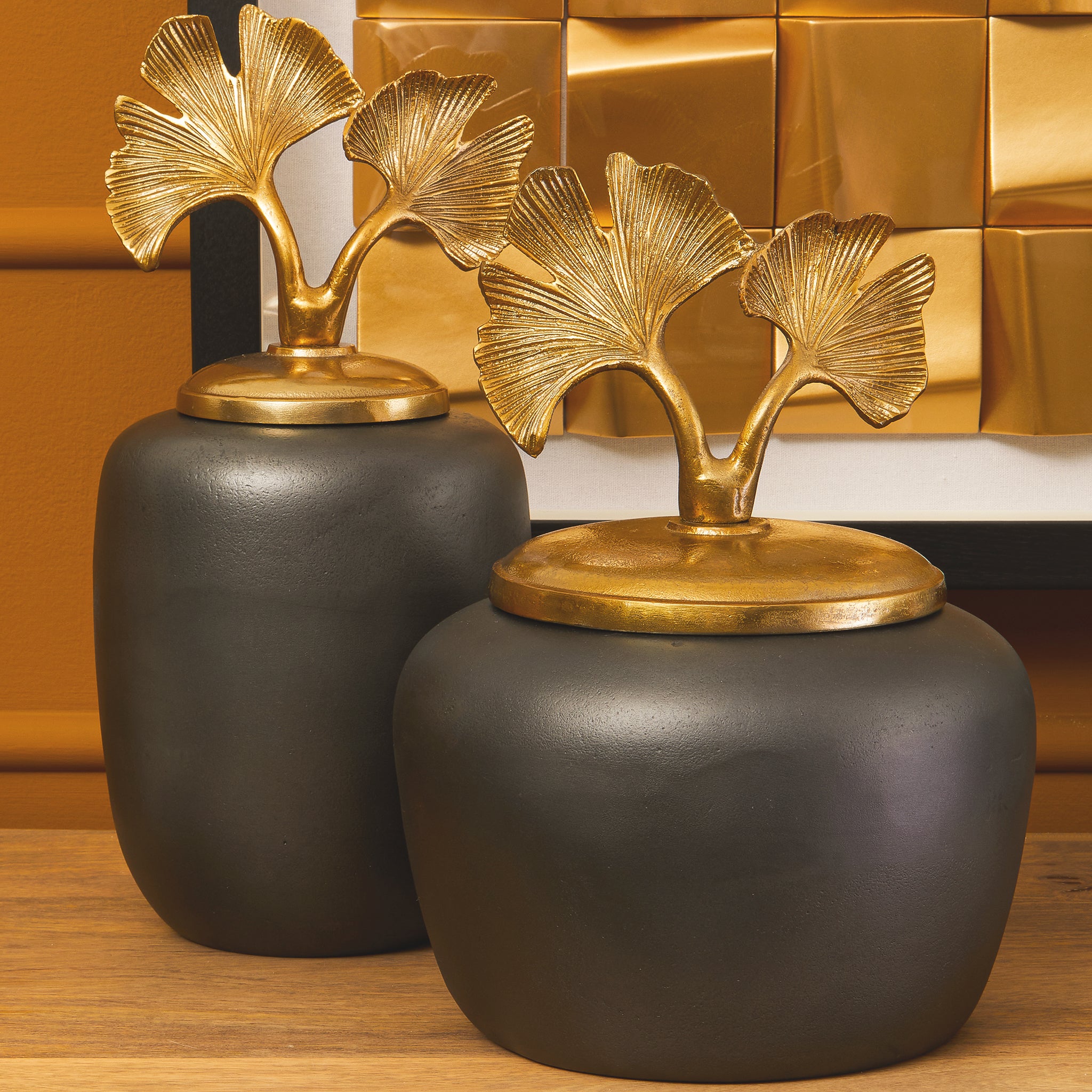Pair of Alix Round Grey Aluminium Ginkgo Leaf Decorative Ginger Jars displayed together, featuring dark grey rounded bodies and statement gold ginkgo leaf lids against a warm interior backdrop.