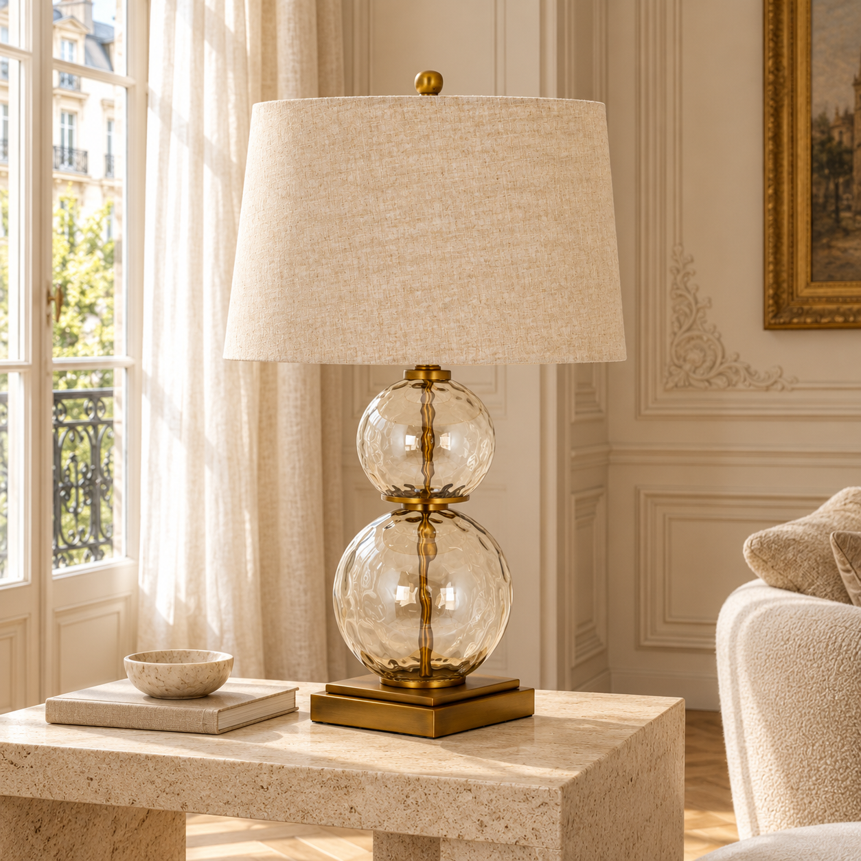 Amélie 70cm clear glass and gold table lamp with linen shade on a stone table in a bright neutral living room.