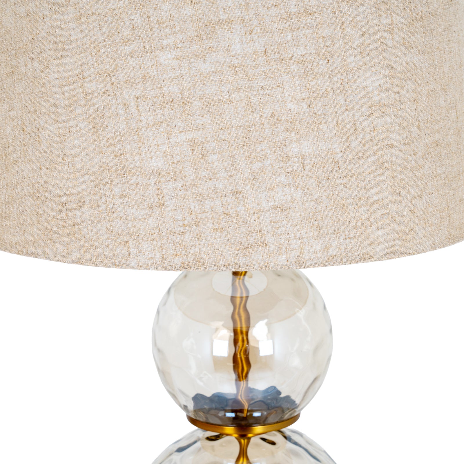Detail of linen lamp shade and upper clear glass globe with gold fittings against a white background.