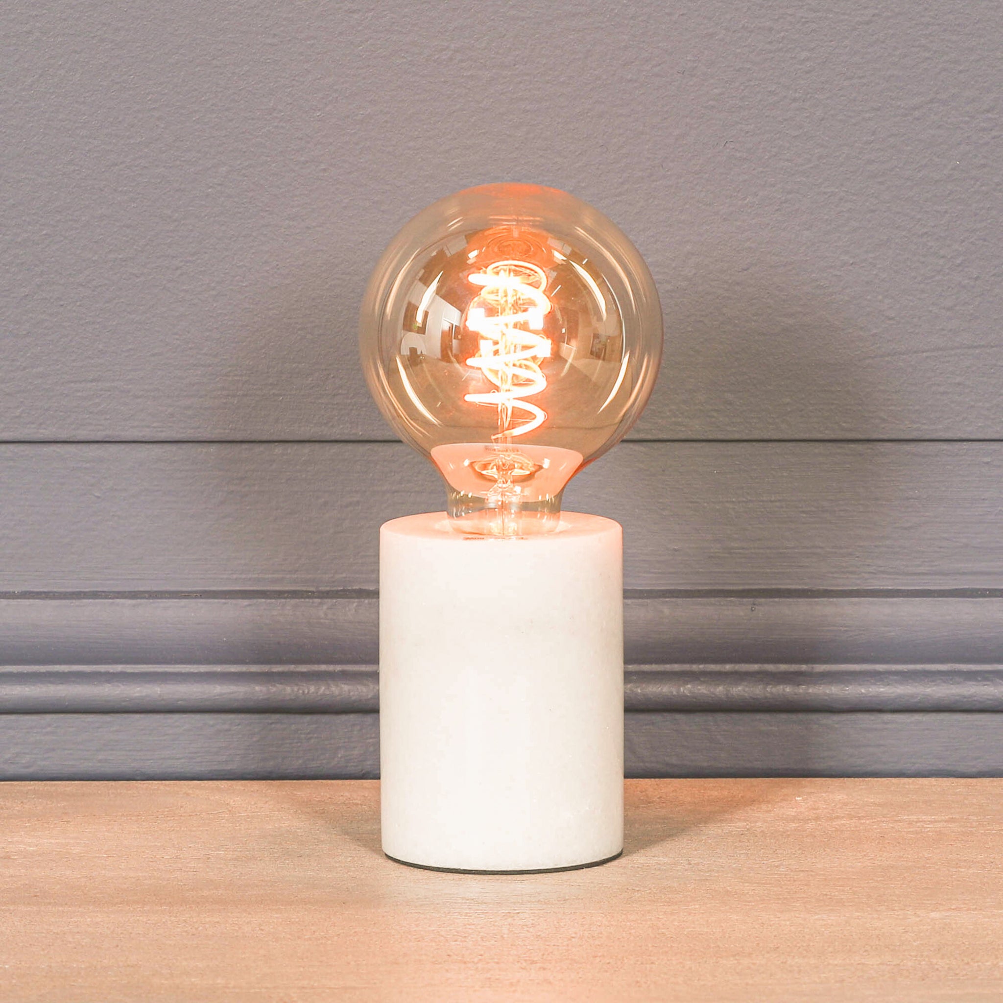 Amélie Industrial White Marble Table Lamp with Braided Cord featuring a polished white marble base and glowing Edison filament bulb, ideal as a bedside lamp, desk lamp or modern accent lighting.