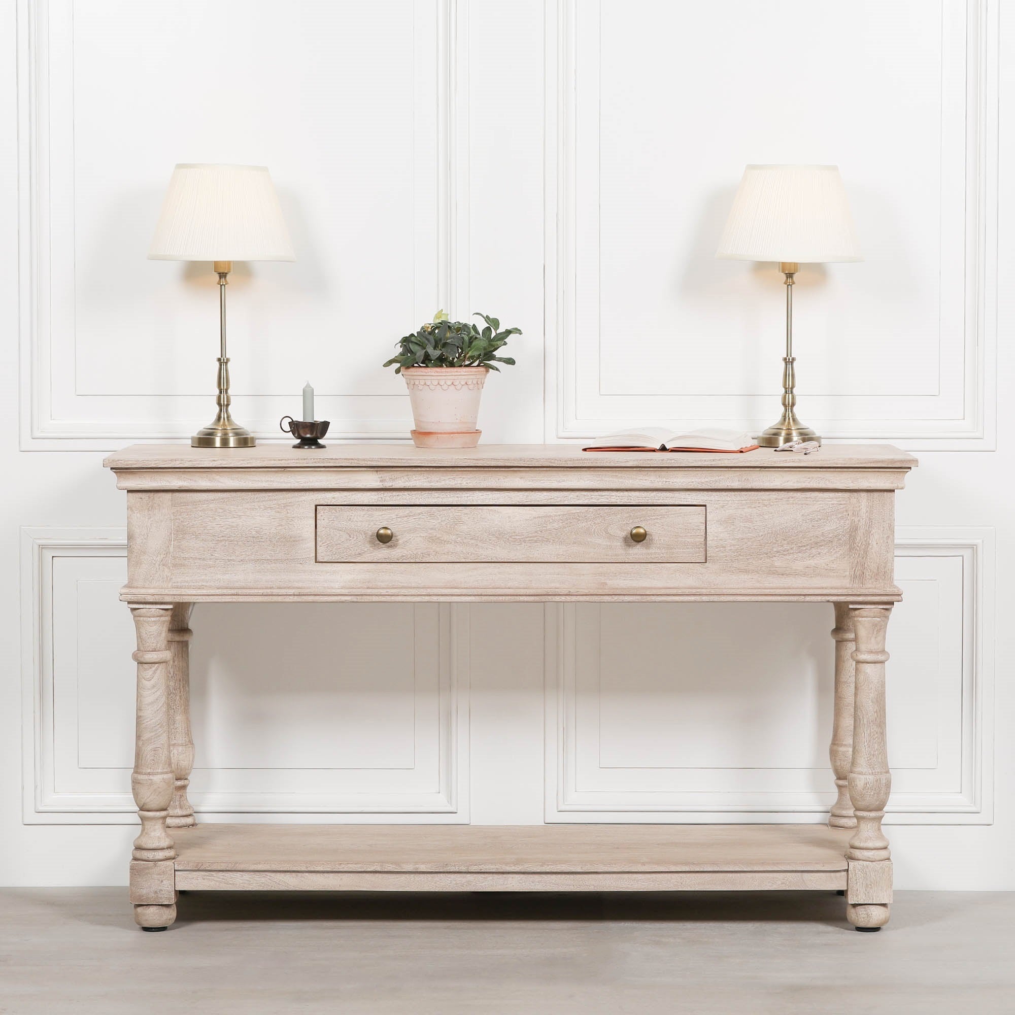 Pair of Amélie Classical satin brass candlestick table lamps with cream pleated shades styled on a light wooden console table with decorative accessories, creating an elegant traditional interior.