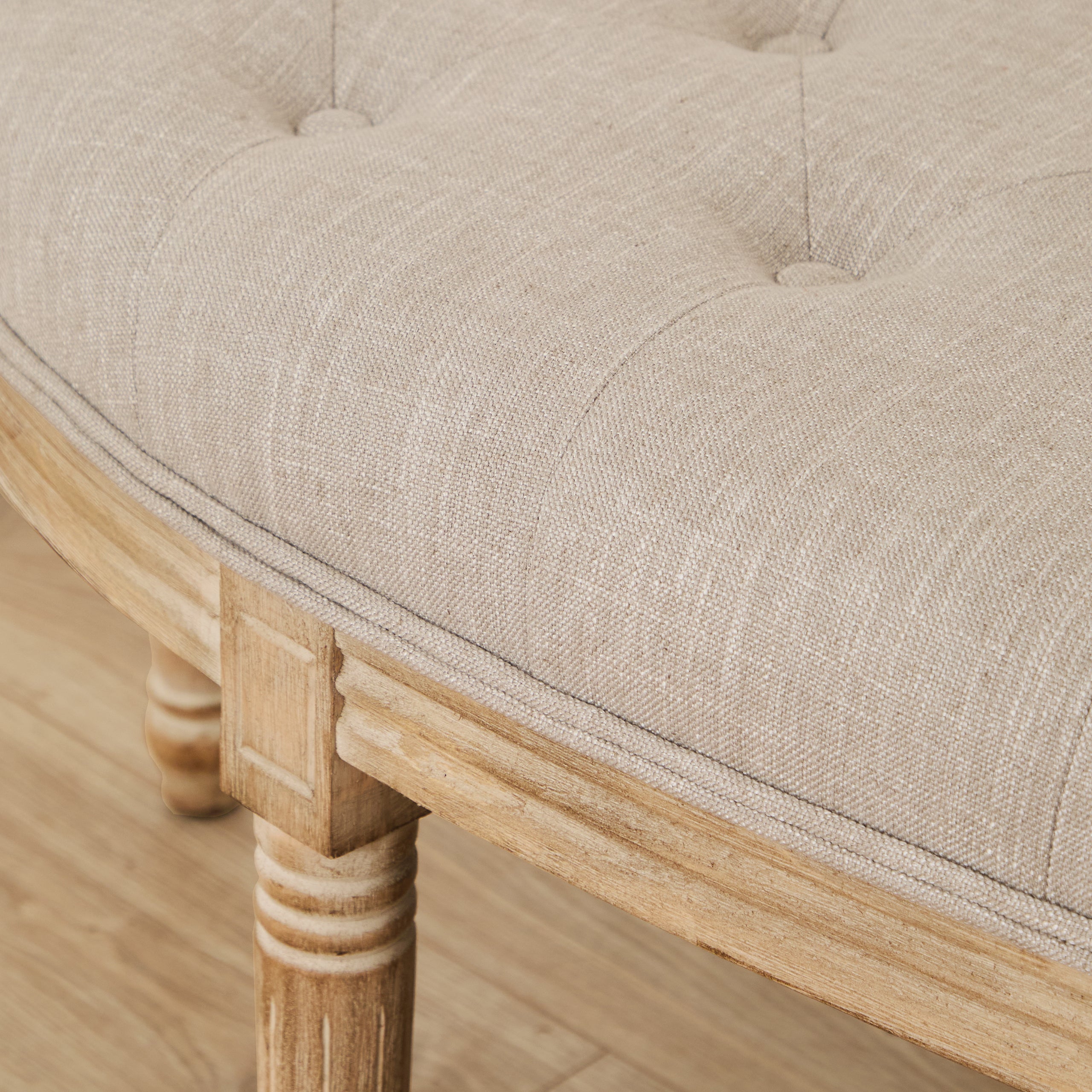 Close-up of Annette bench showing cream tufted upholstery and natural wood frame above light wood flooring.
