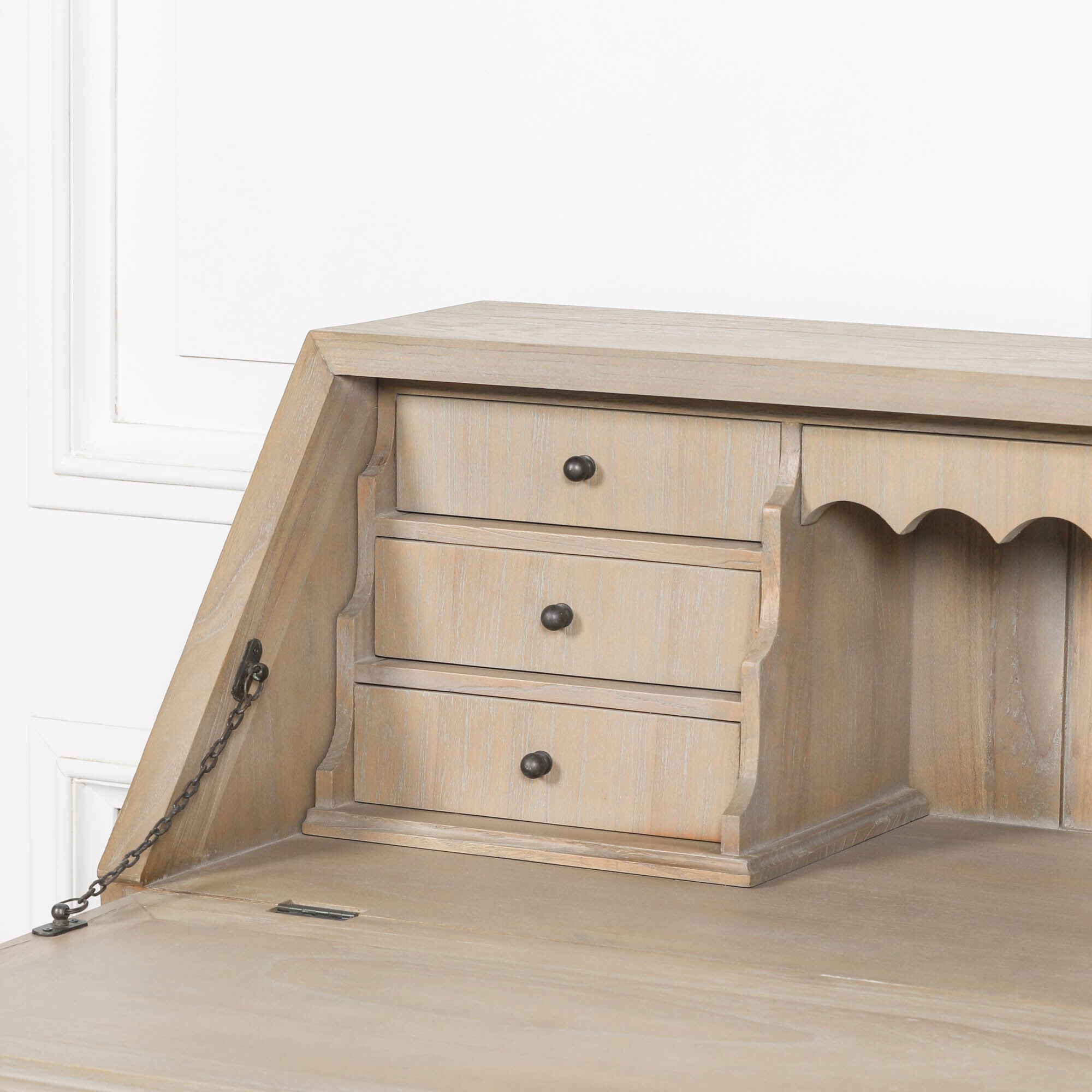 Armand white cedar bureau desk close-up showing three drawers, scalloped detail and chain against a white wall.