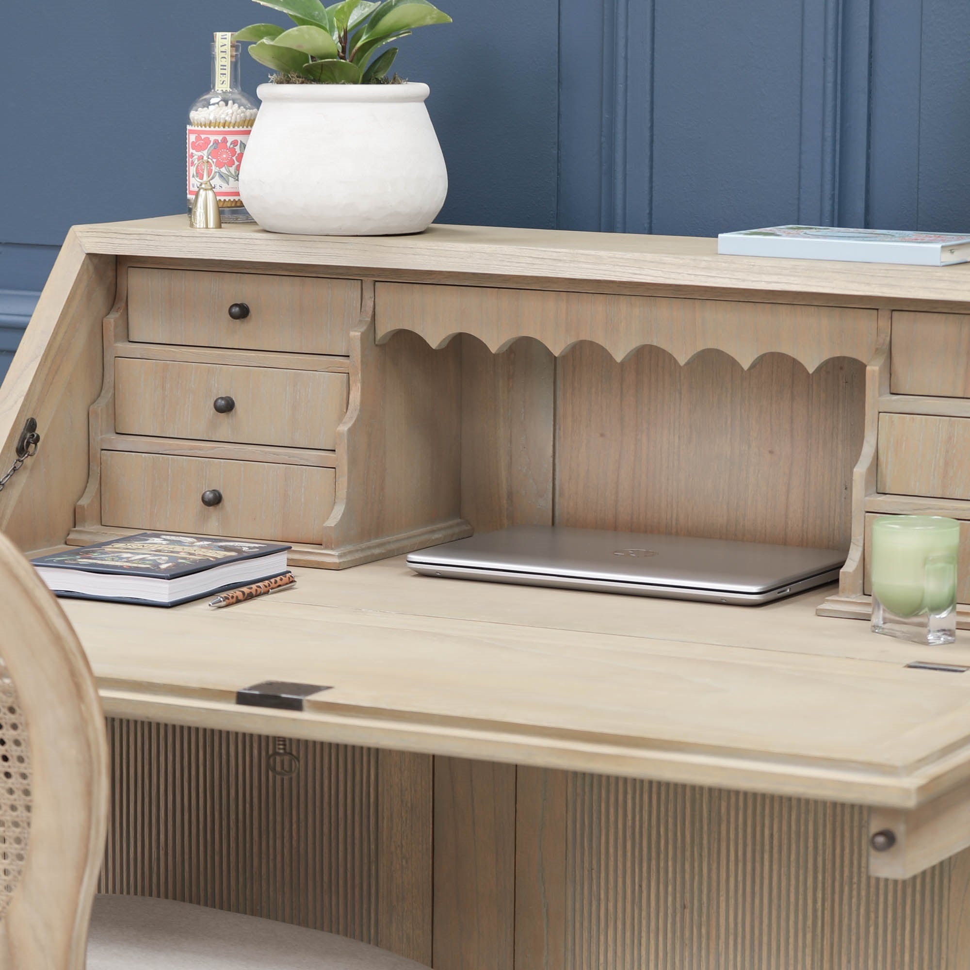 Armand white cedar bureau desk close-up with laptop, drawers and scalloped detail against a blue panelled wall.
