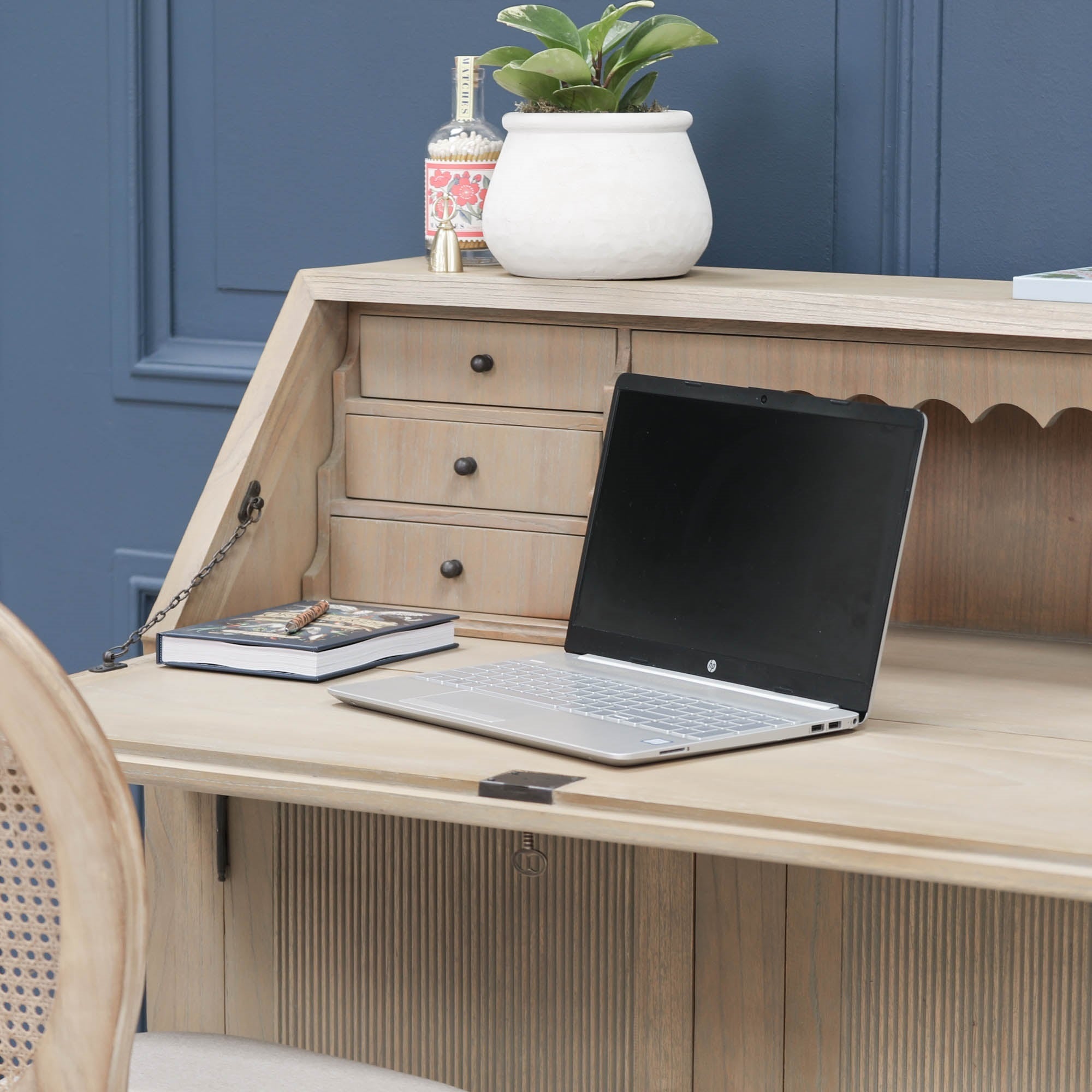 Armand white cedar bureau writing desk open with laptop, drawers and chair against a blue panelled wall.