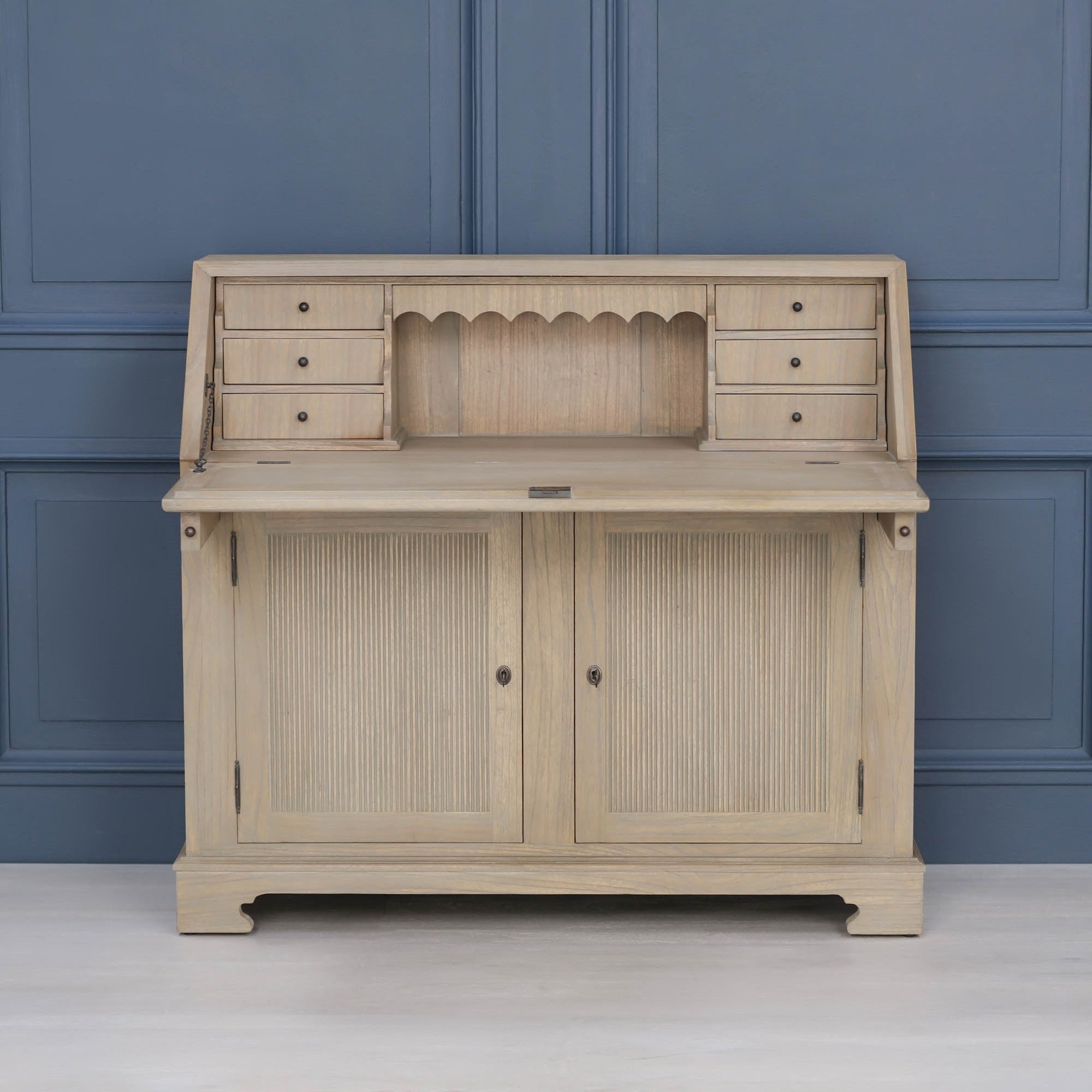 Armand white cedar bureau writing desk open with drawers and reeded storage doors against a blue panelled wall.