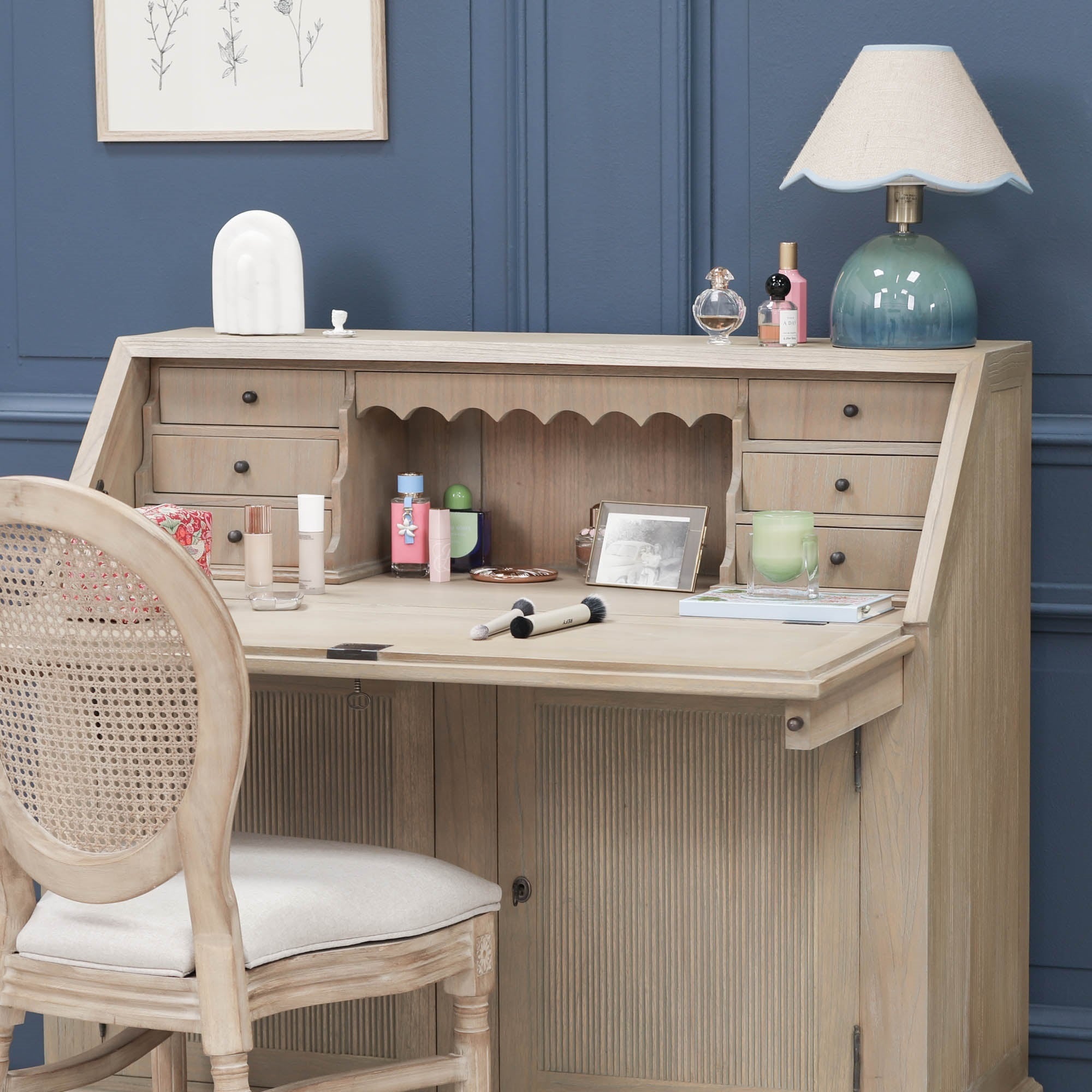 Armand white cedar bureau writing desk styled as a vanity with chair and storage against a blue panelled wall.