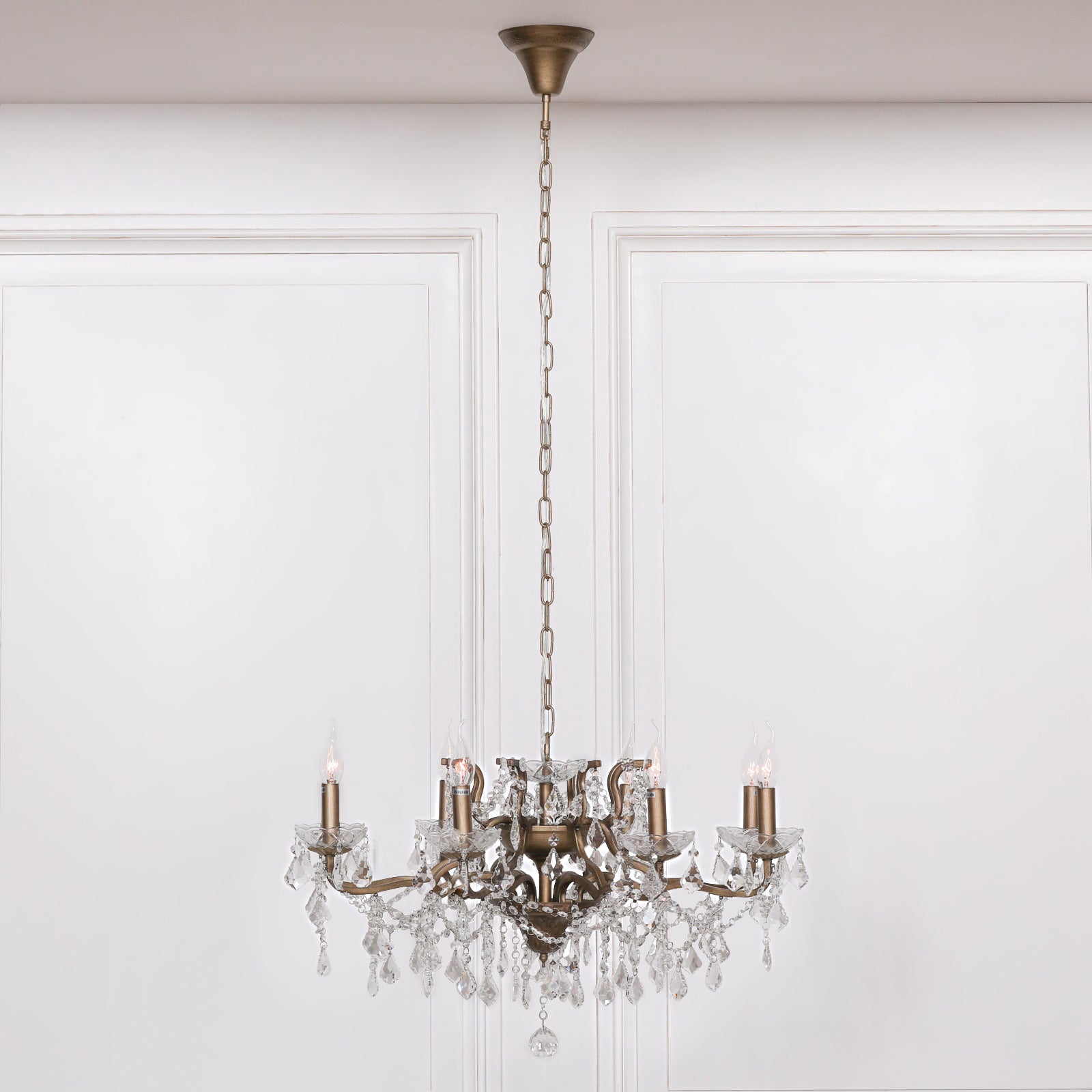 Aubert gold 8 light chandelier suspended by chain against a white panelled wall.