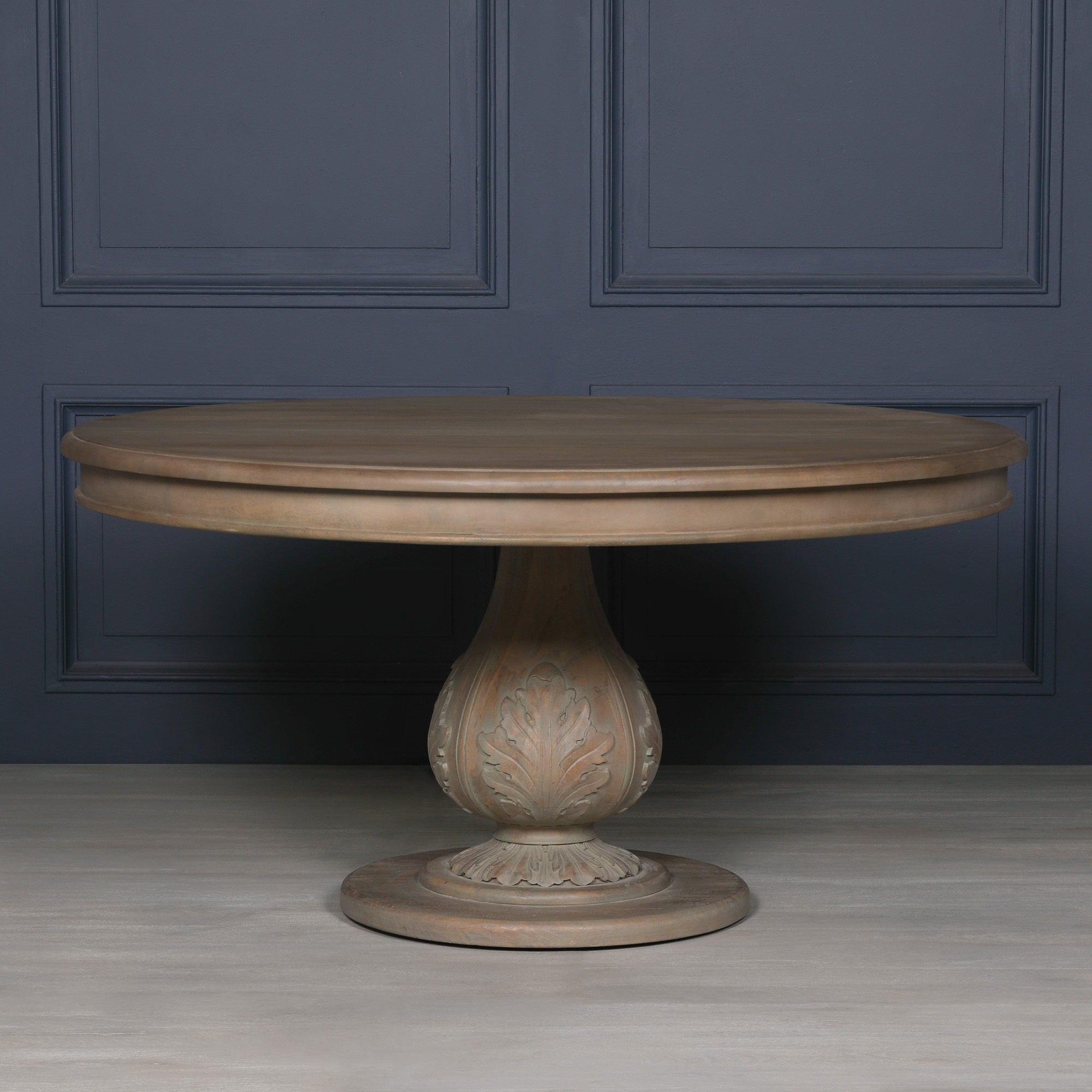 Auguste Round Acorn Pedestal Dining Table 150cm for 6 in Rustic Washed Hardwood displayed against a dark blue panelled wall, highlighting the statement carved acorn pedestal base, spacious round tabletop and luxury farmhouse dining room styling.