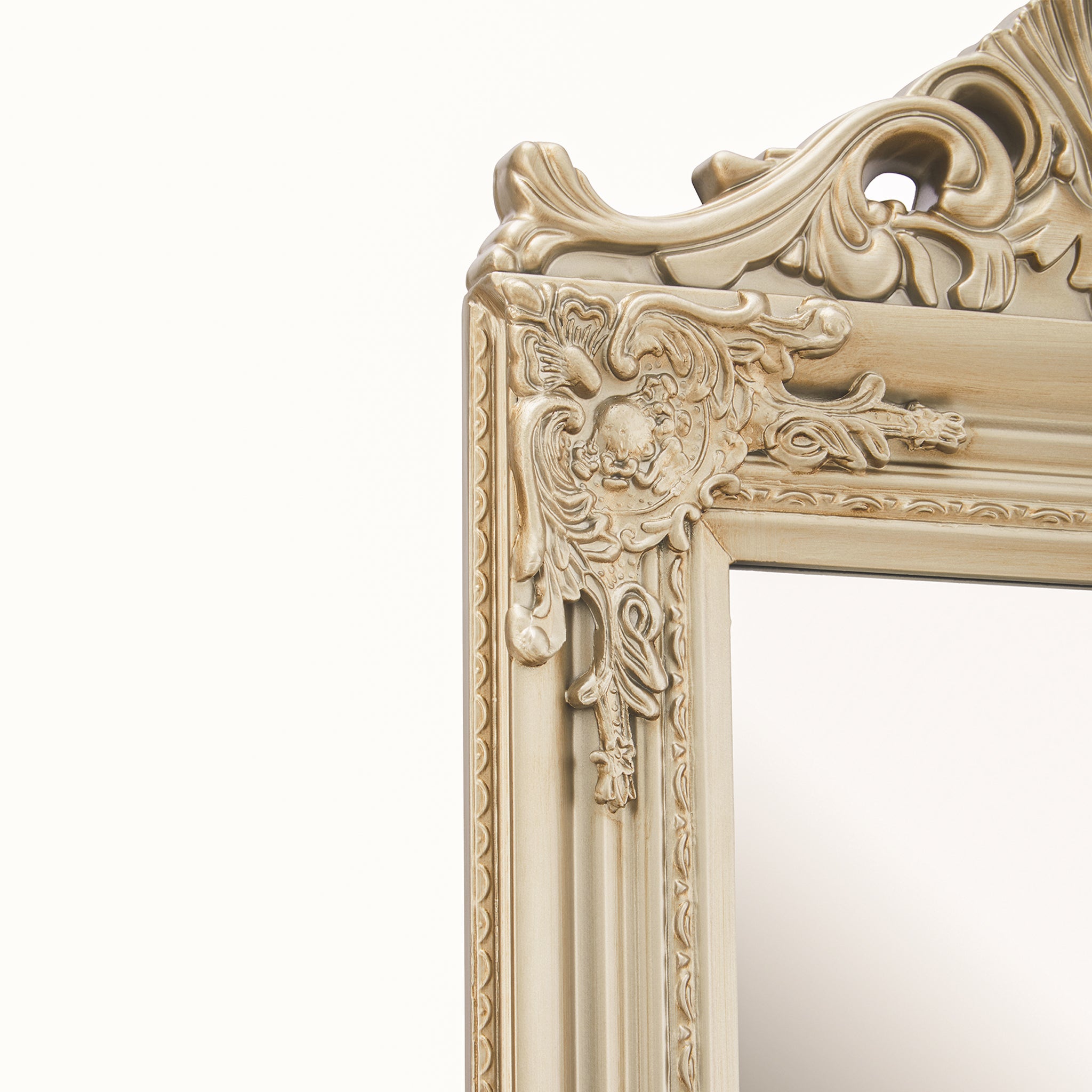 Close-up of the Aurelia French-style floor mirror frame, showing elaborate carved-effect floral scrollwork, moulded edging and champagne gilded detailing around the upper corner.