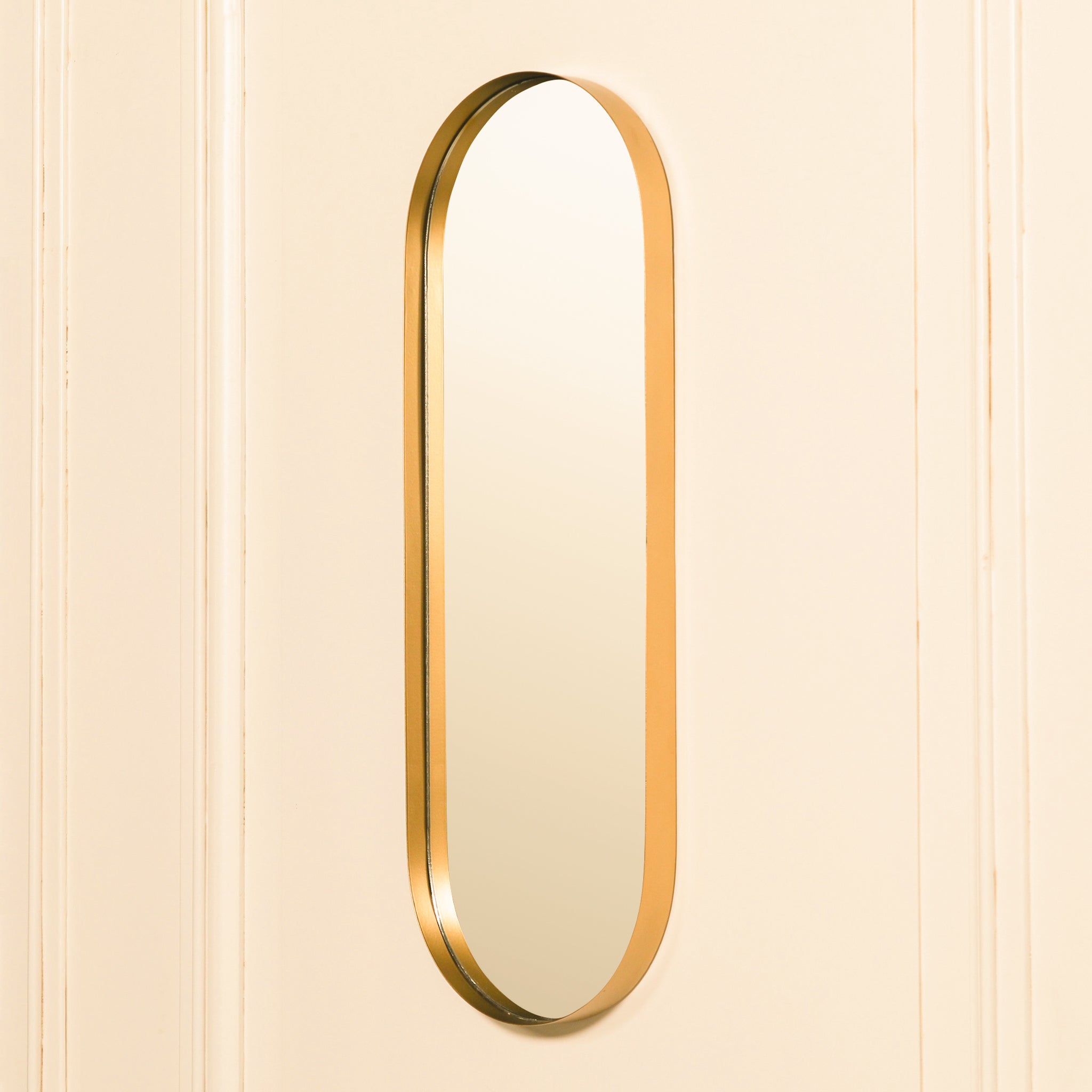 Aurelia Gold Oval Accent Wall Mirror displayed on a light panelled wall, featuring a slim elongated oval silhouette and distinctive deep-set gold frame in a contemporary interior setting.