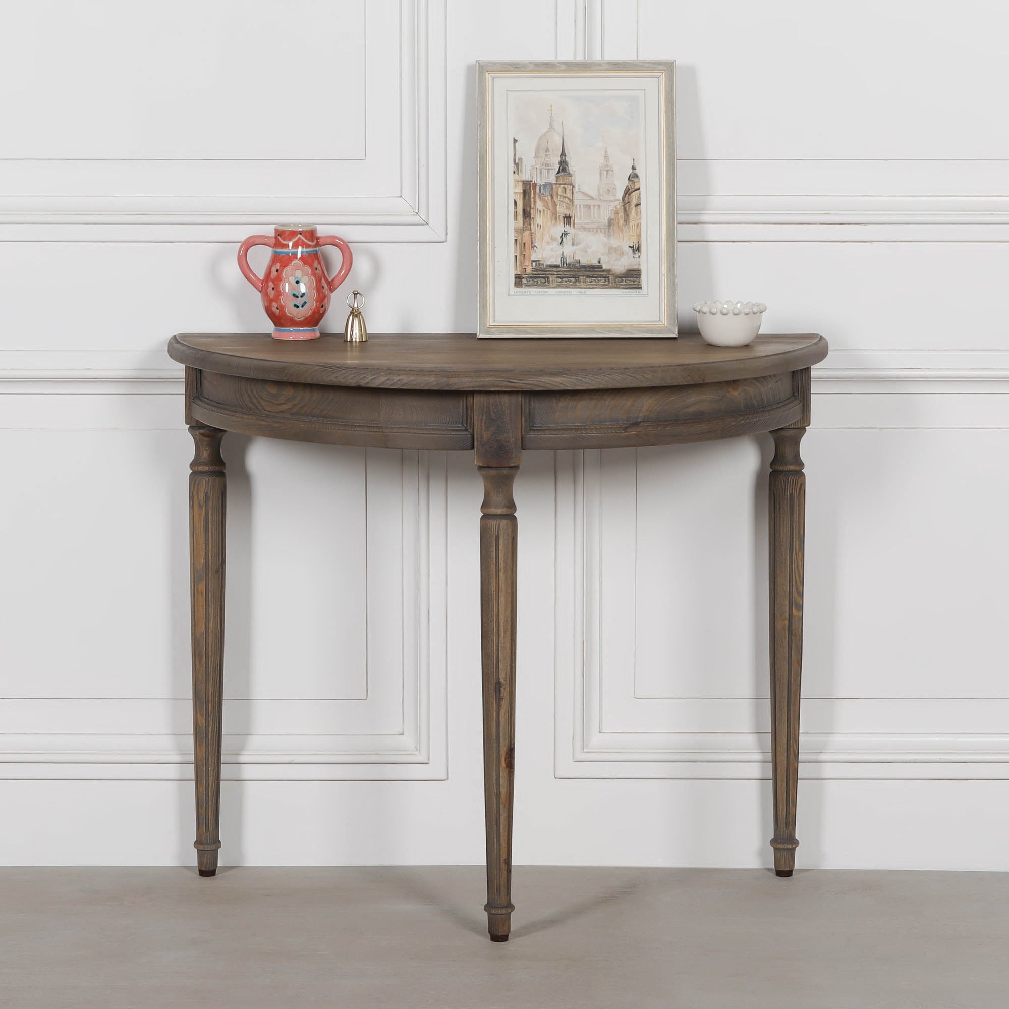 Aveline rustic pine hallway console table with demi-lune top and turned legs, styled against a white panelled wall.