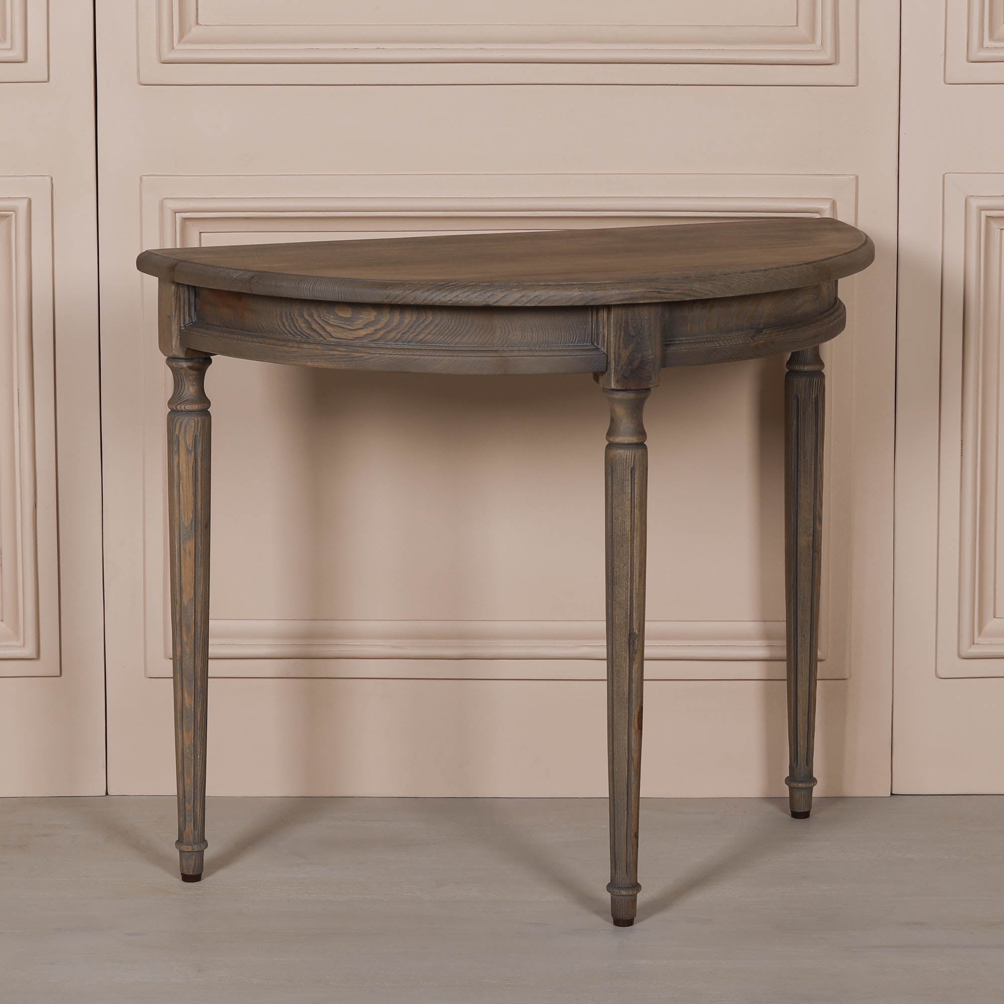 Angled view of Aveline rustic pine wood demi-lune console table with curved top, distressed finish and turned legs.