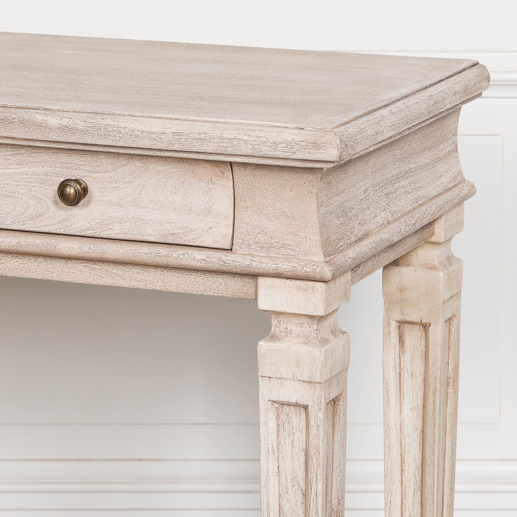 Close-up of Camille acacia wood breakfront console table drawer, brass knob and leg against a white panelled wall