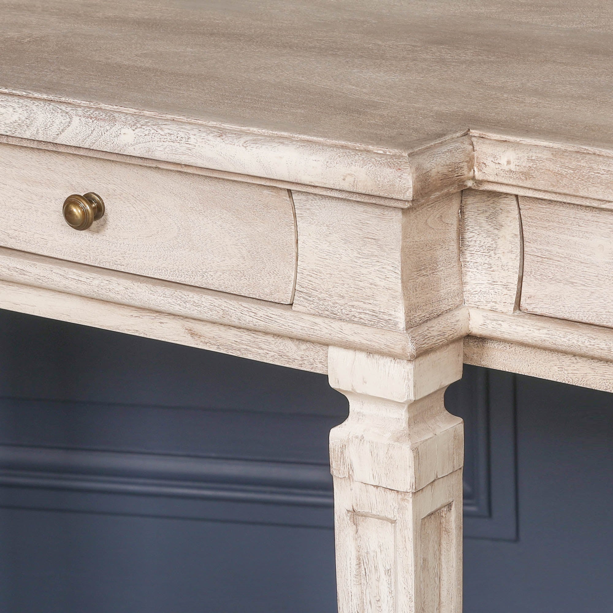 Camille acacia wood breakfront console table drawers and brass knob detail against a dark blue panelled wall
