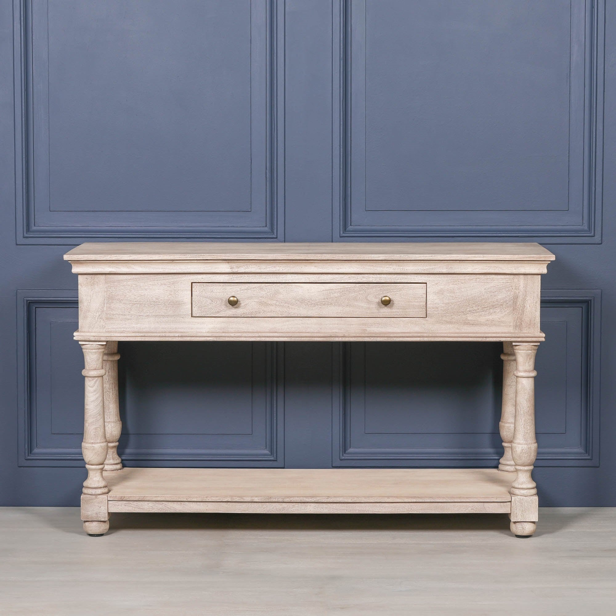 Camille acacia wood console table with drawer, turned legs and lower shelf against a dark blue panelled wall