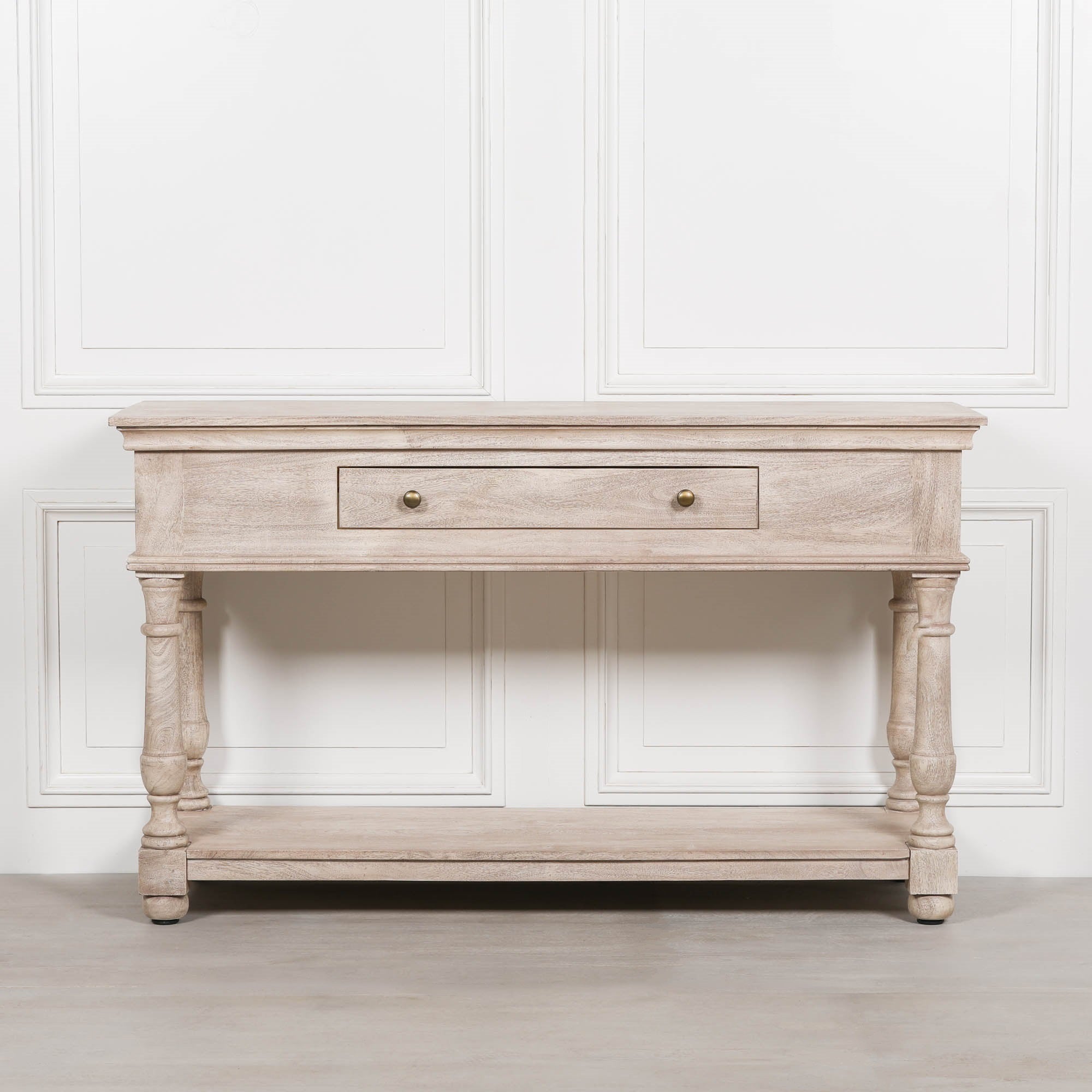 Front view of Camille acacia wood console table with drawer and lower shelf against a white panelled wall