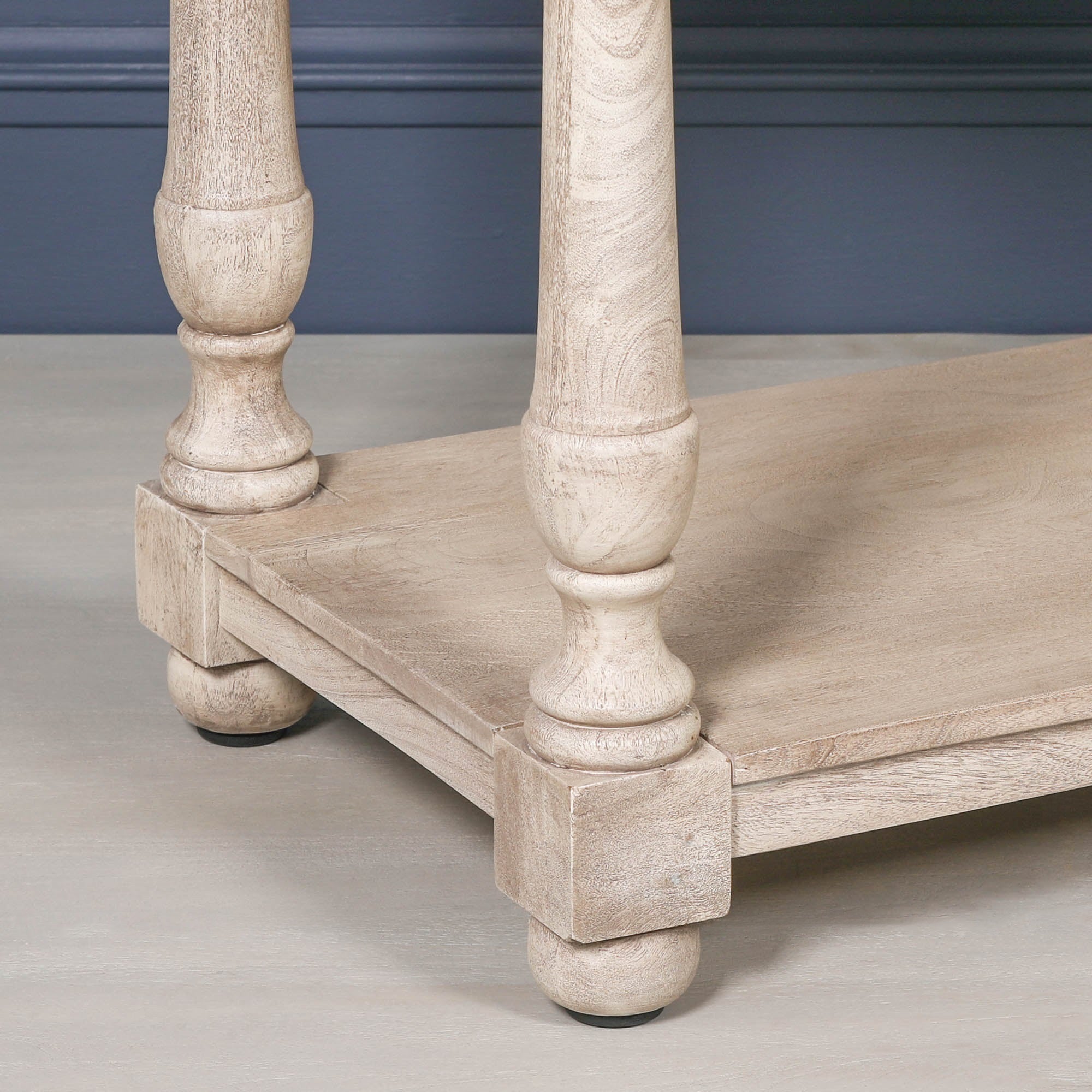Camille acacia console table detail showing turned legs and lower shelf against a dark blue panelled wall