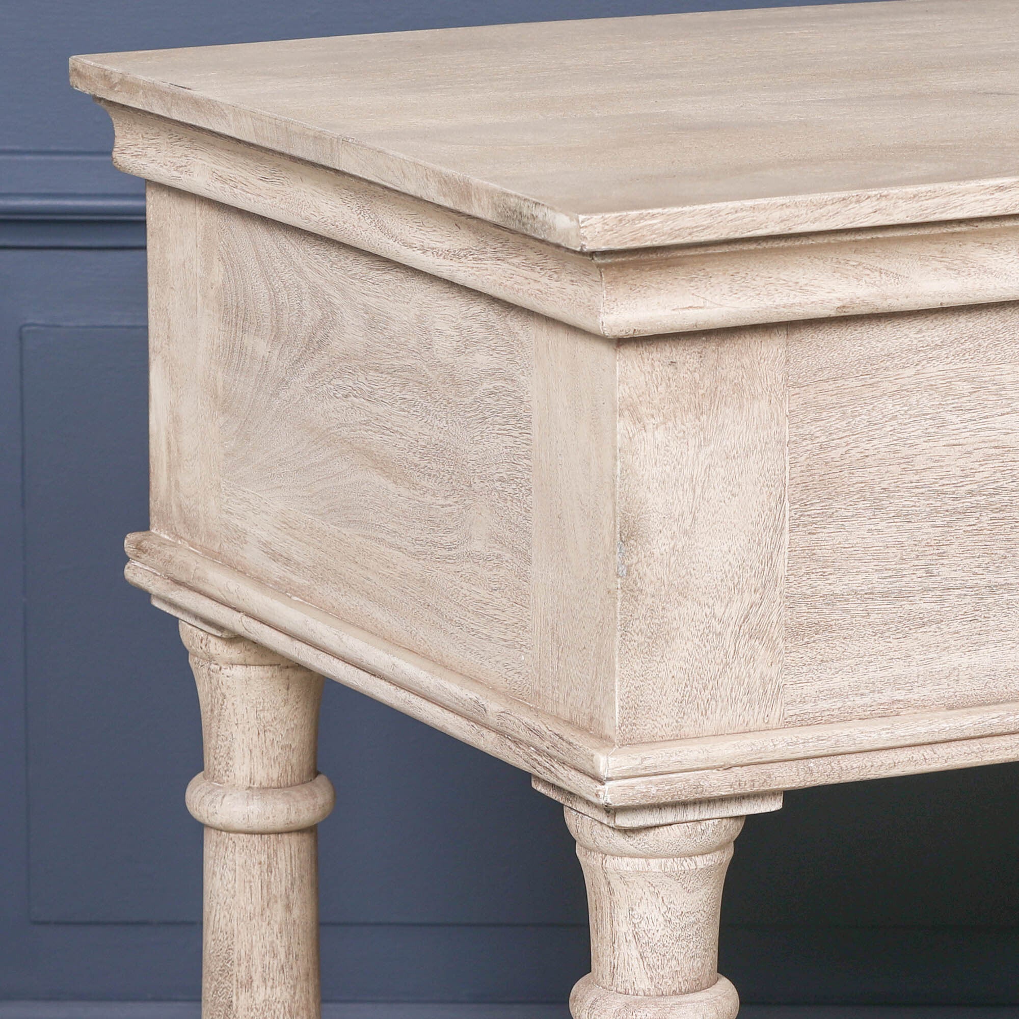 Close-up of Camille acacia wood console table top and grain detailing against a dark blue panelled wall