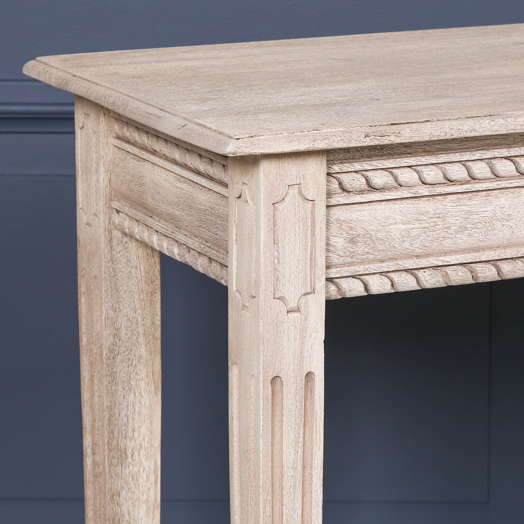 Close-up of Camille acacia wood dressing table with carved rope trim and leg against a dark blue panelled wall
