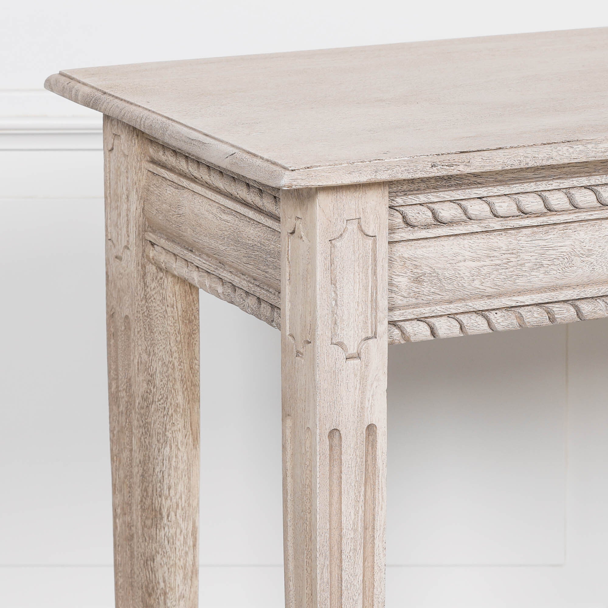 Close-up of Camille acacia wood dressing table with carved rope trim and leg against a white panelled wall