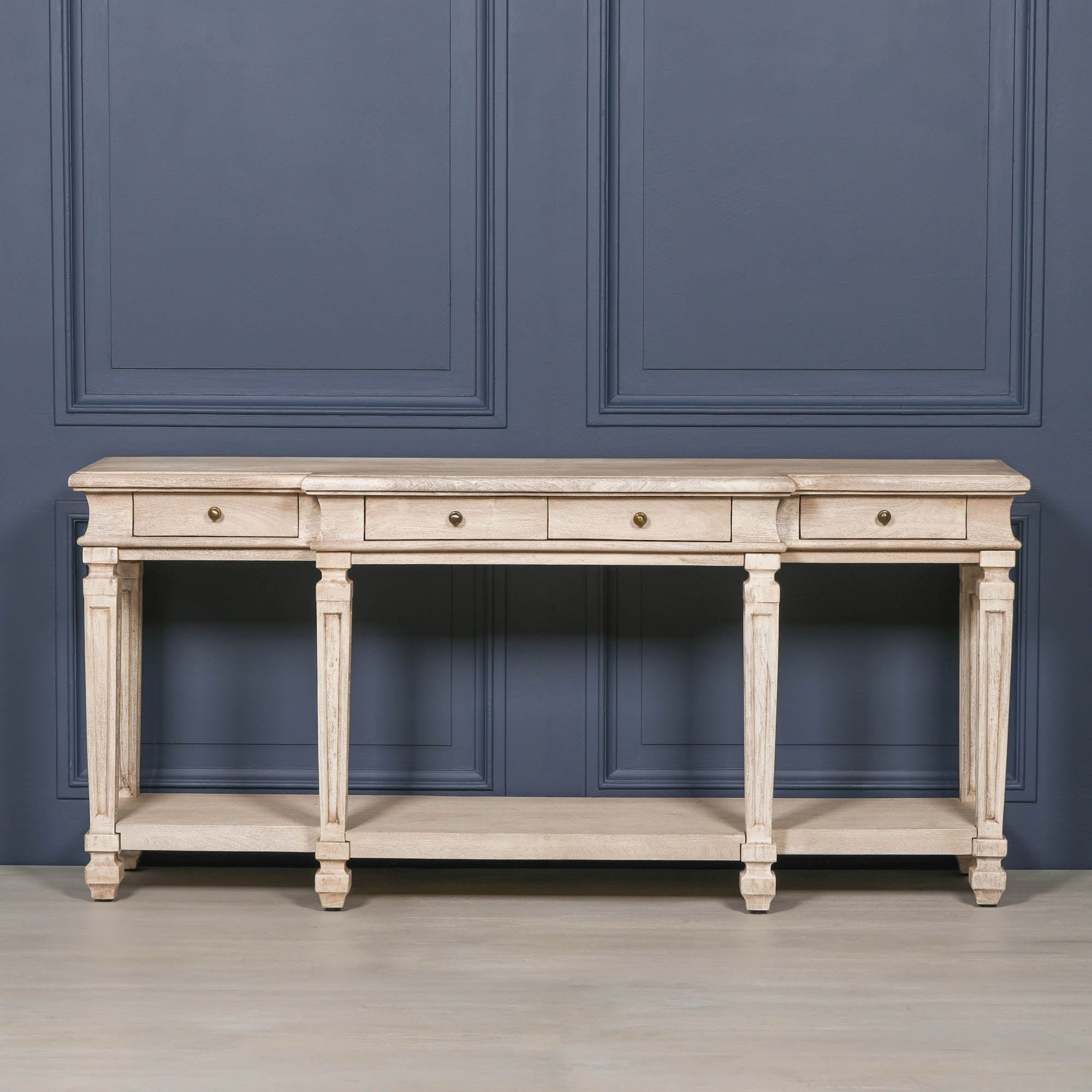Camille acacia wood 4 drawer breakfront console table with lower shelf against a dark blue panelled wall