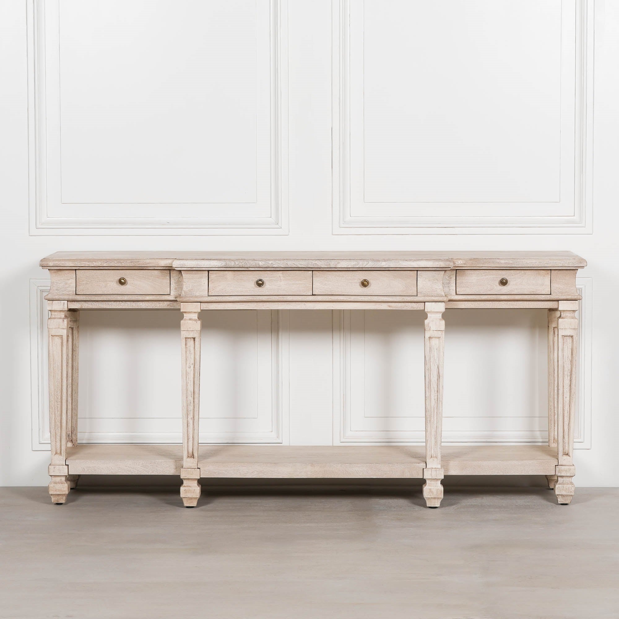Camille acacia wood 4 drawer breakfront console table with lower shelf against a white panelled wall