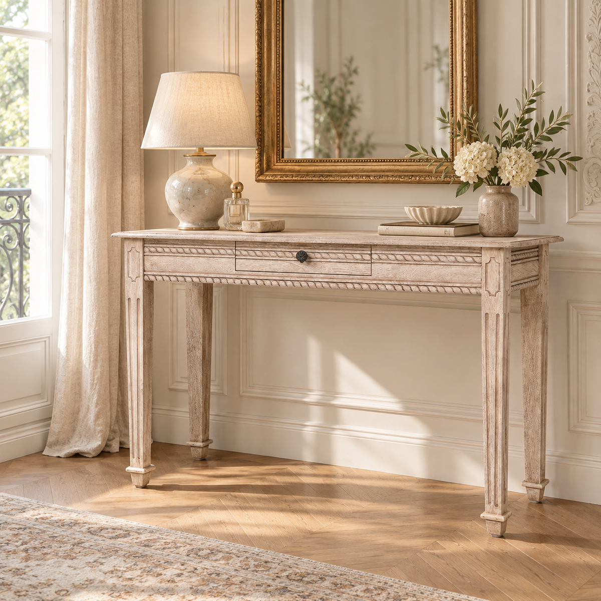 Camille acacia wood dressing table with carved detail and drawer, styled by a window with gold mirror, lamp and flowers