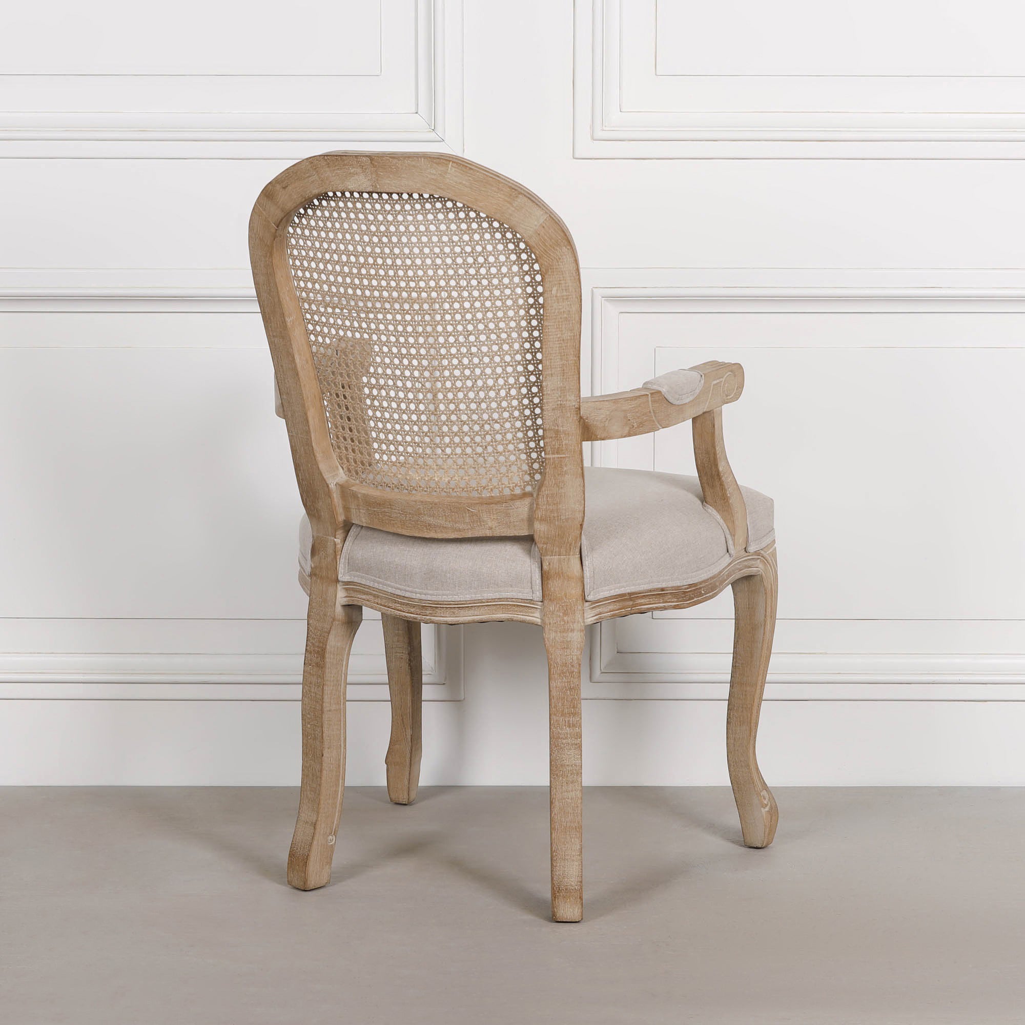 Rear view of Camille birch wood dining armchair showing woven cane back against a white panelled wall