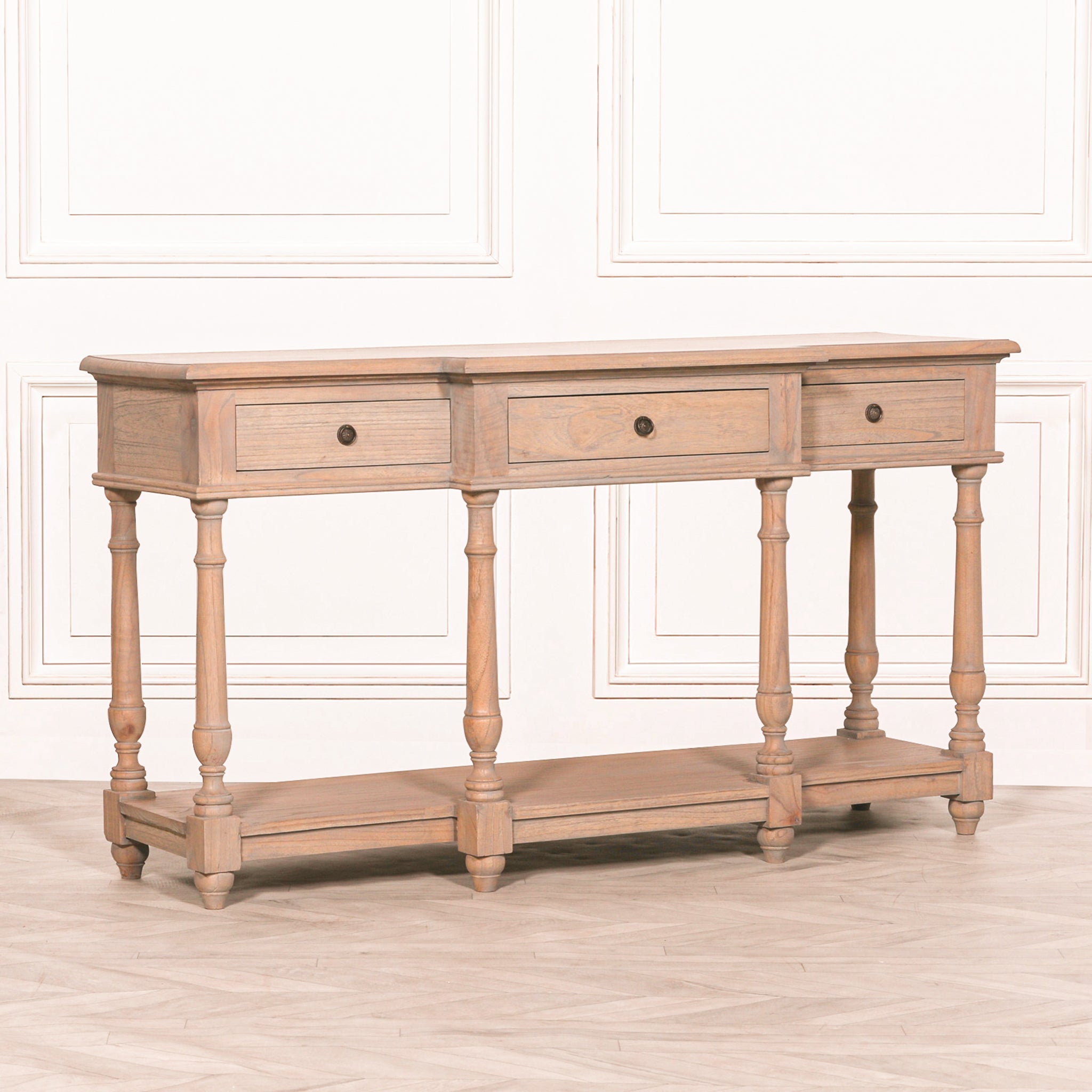 Angled perspective of the Camille Breakfront white cedar wood console table with three drawers, showcasing the rustic finish, elegant turned legs, handcrafted construction and lower display shelf.