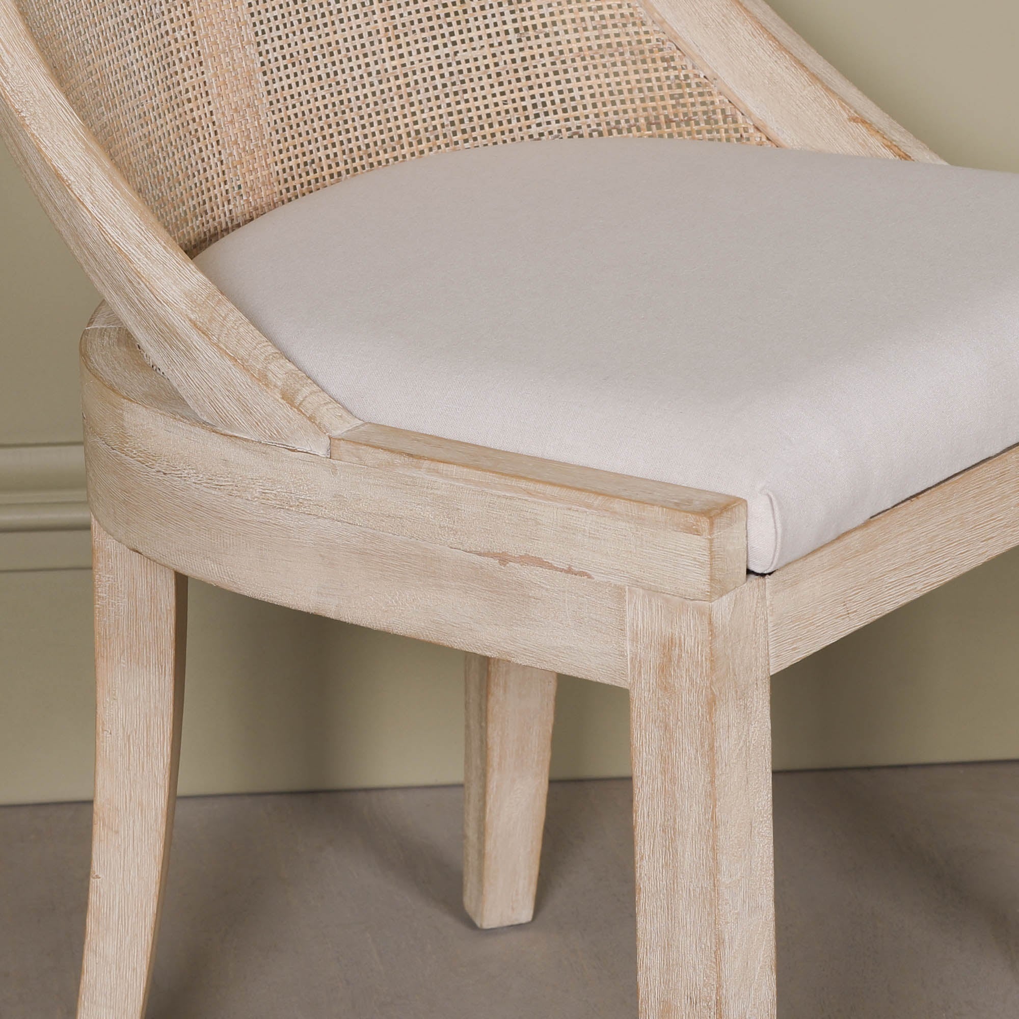 Close-up of the Camille Cane Back Dining Chair featuring the beige linen upholstered seat cushion, natural woven cane backrest and washed birch wood frame, highlighting premium craftsmanship and refined detailing.