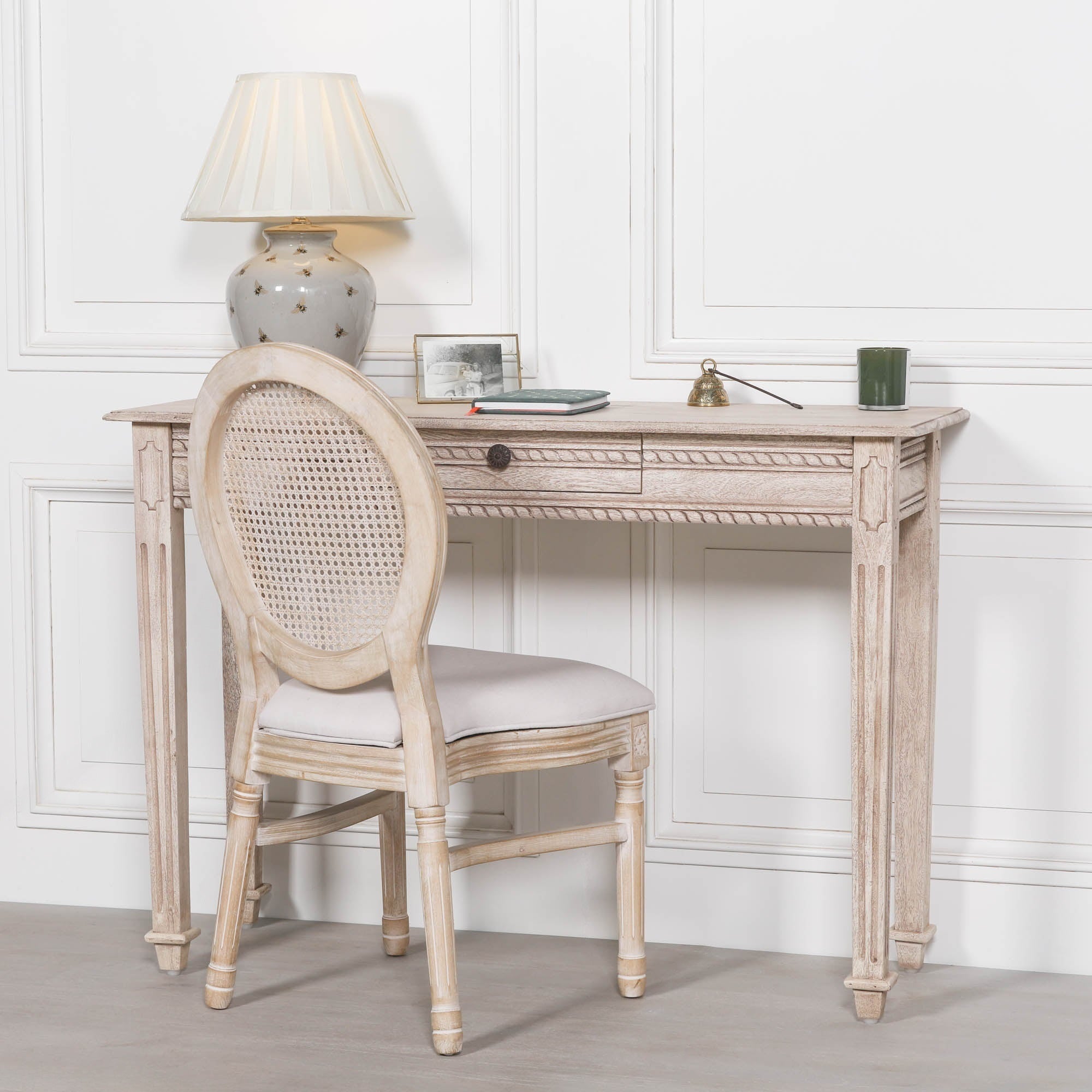 Camille carved acacia wood dressing table styled with rattan chair and lamp against a white panelled wall