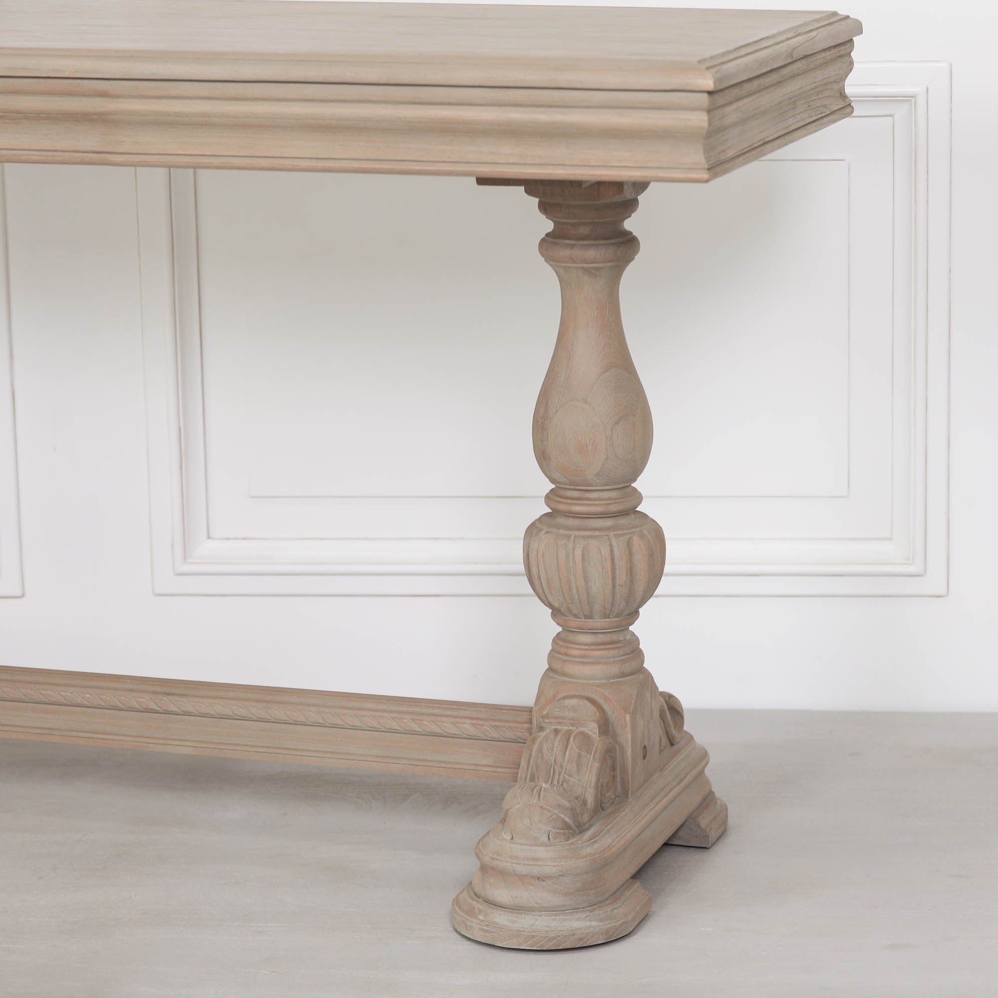 Close-up of Camille carved cedar console table leg and stretcher in a rustic white finish against a white wall.