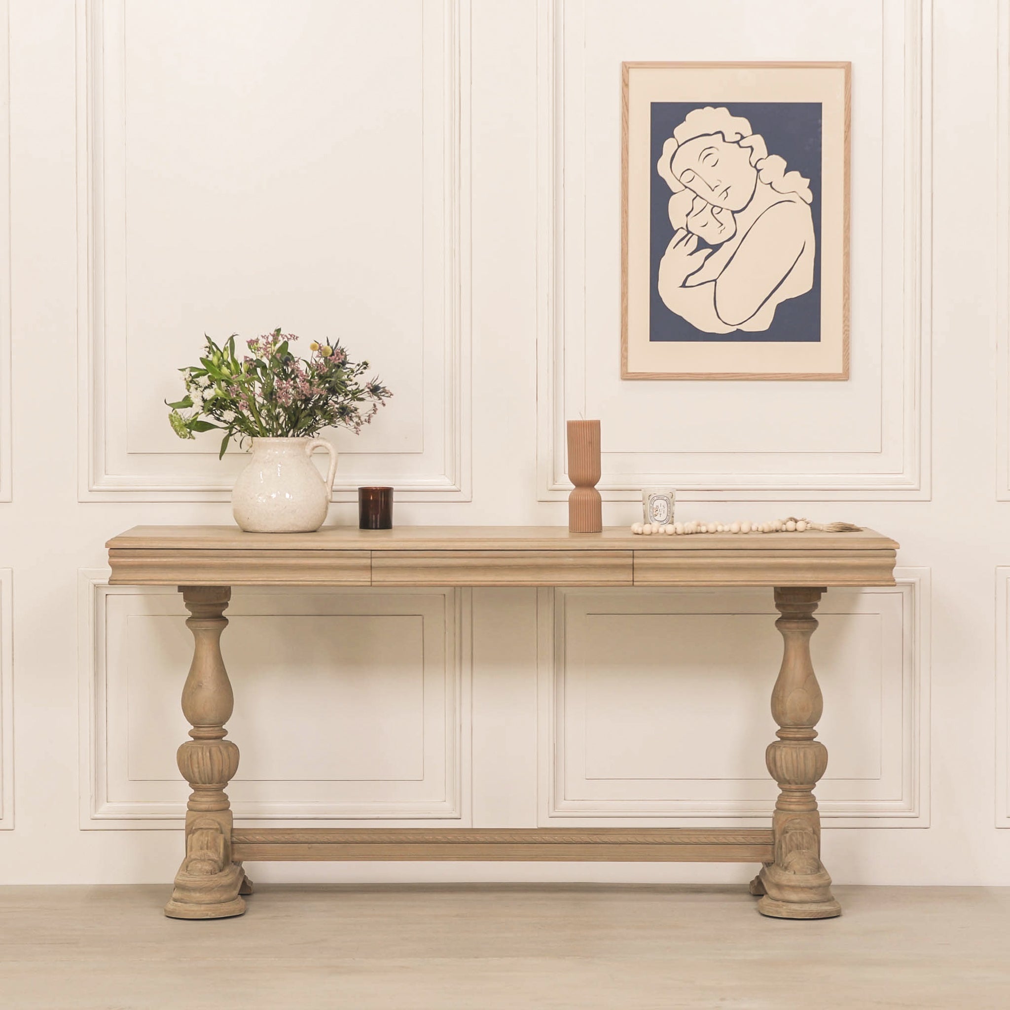 Camille Carved White Cedar Wood Console Table with Drawer styled with decorative vases, flowers and artwork, highlighting its rustic white cedar wood finish and elegant French farmhouse aesthetic for luxury interiors.