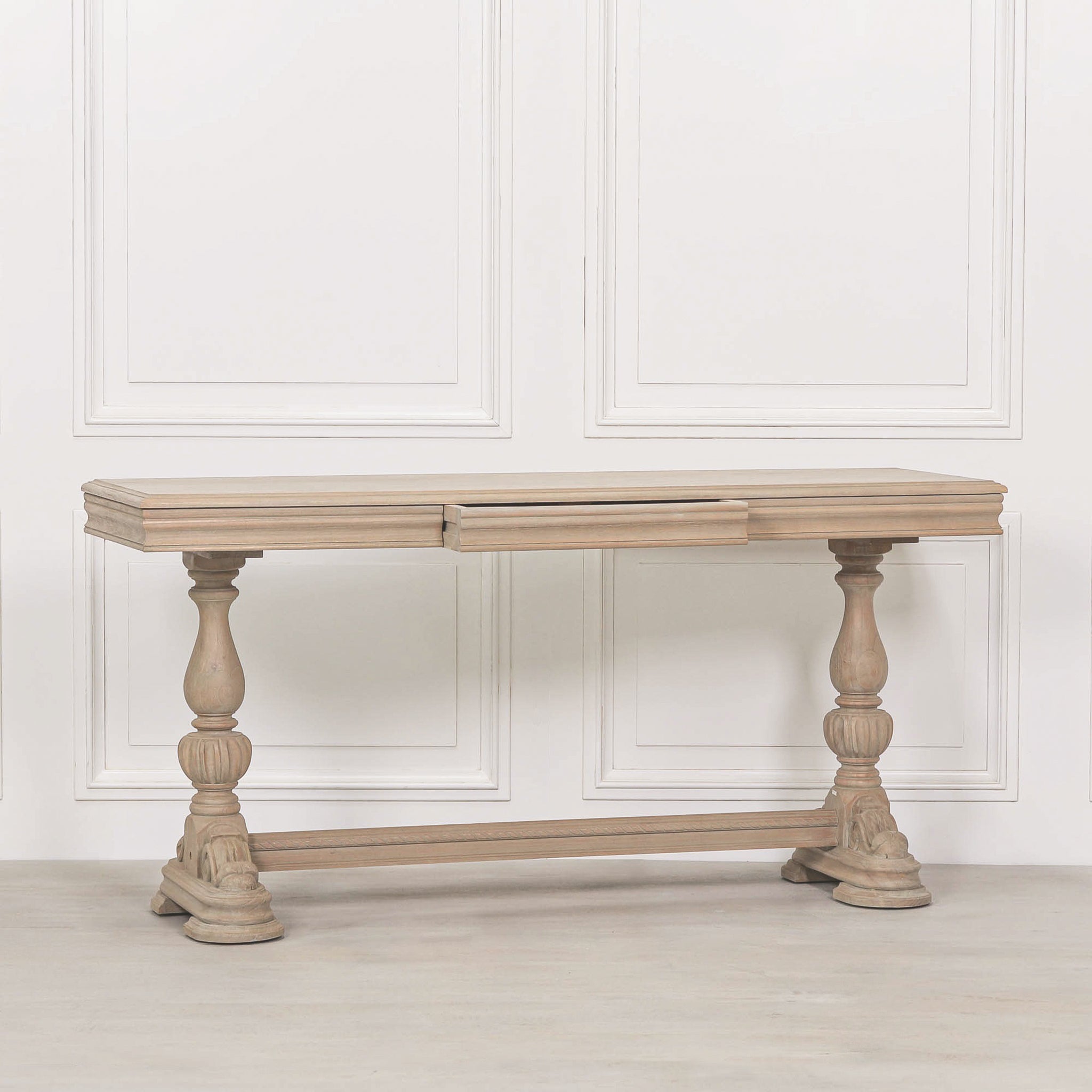 Camille Carved White Cedar Wood Console Table with Drawer displayed against a white panelled wall, showcasing the rustic wood grain, carved turned legs and classic French-inspired console table design.