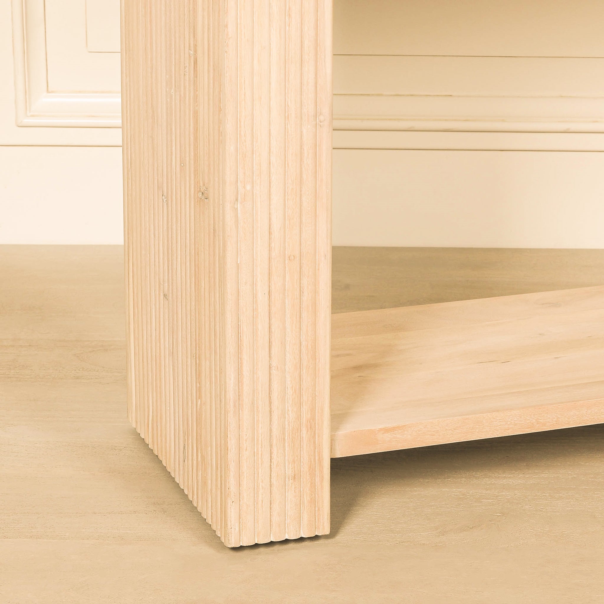 Close-up of the Camille console table showing the vertically fluted acacia wood leg, natural wood grain and full-width lower shelf in a light bleached washed finish.
