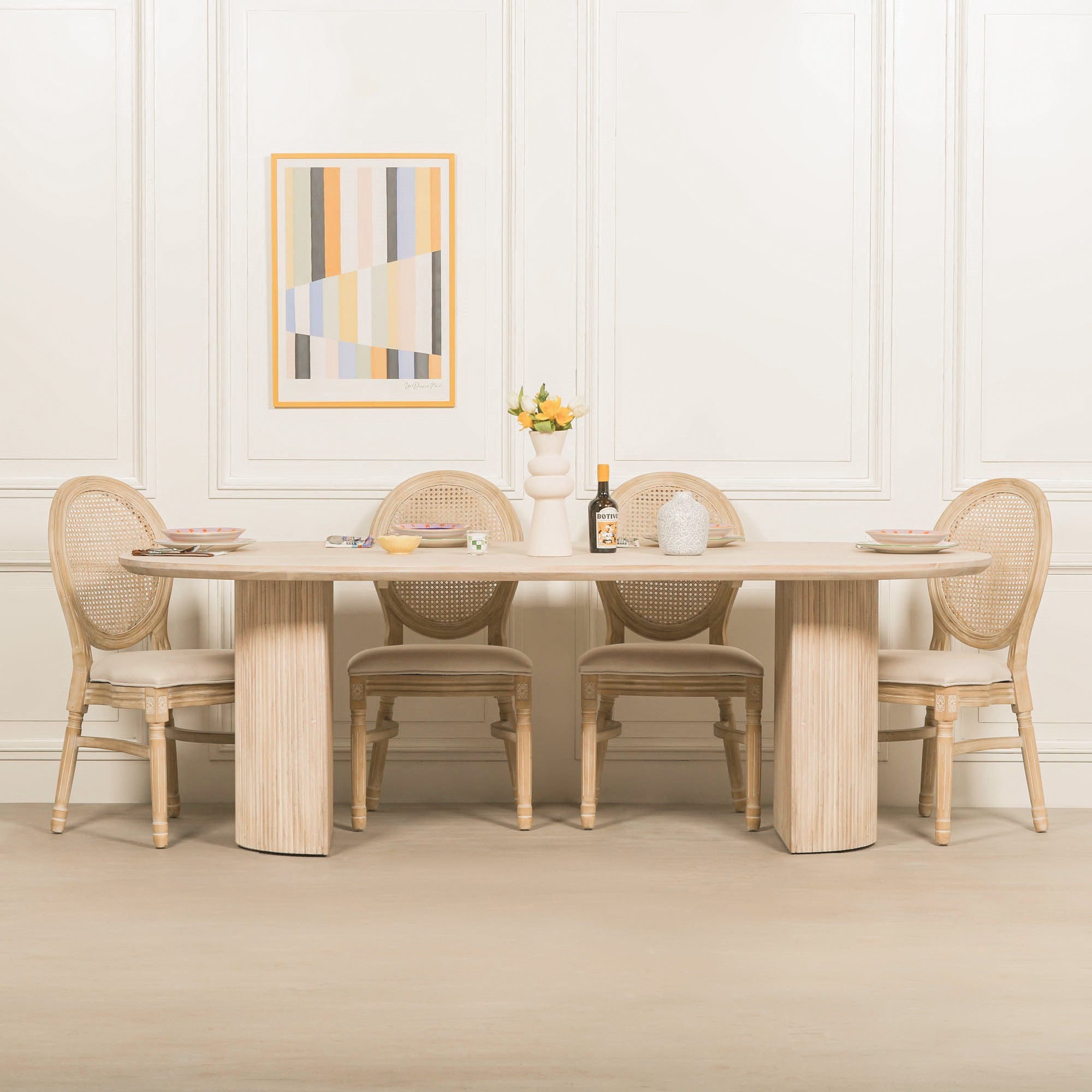 Camille Fluted Acacia Wood Oval 6 Seater Dining Table styled with woven rattan dining chairs in a bright contemporary dining room, highlighting the bleached washed acacia wood finish, oval tabletop and sculptural fluted pedestal design.
