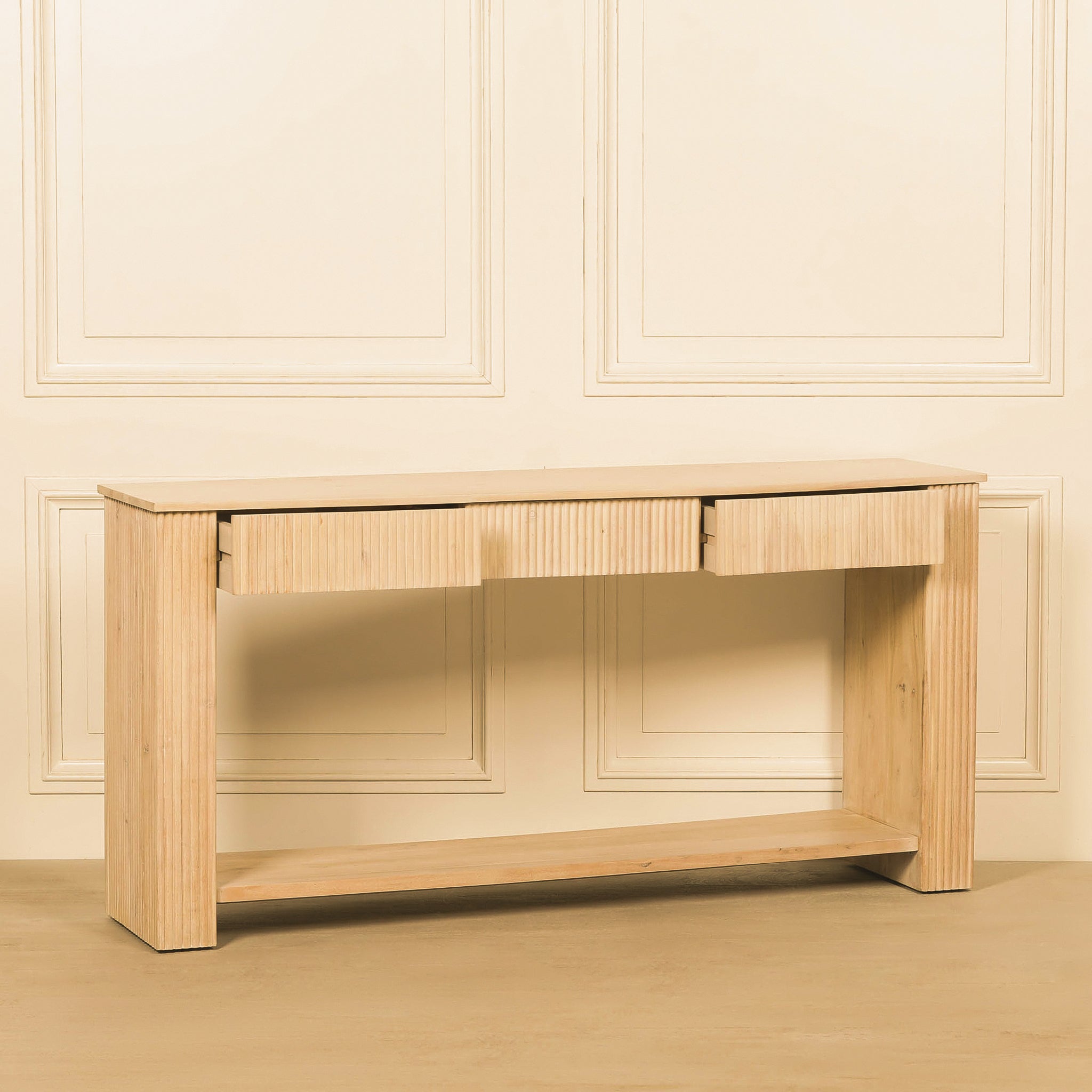 Front lifestyle view of the Camille fluted console table with three drawers open, showing the light bleached washed acacia wood finish and long lower display shelf.