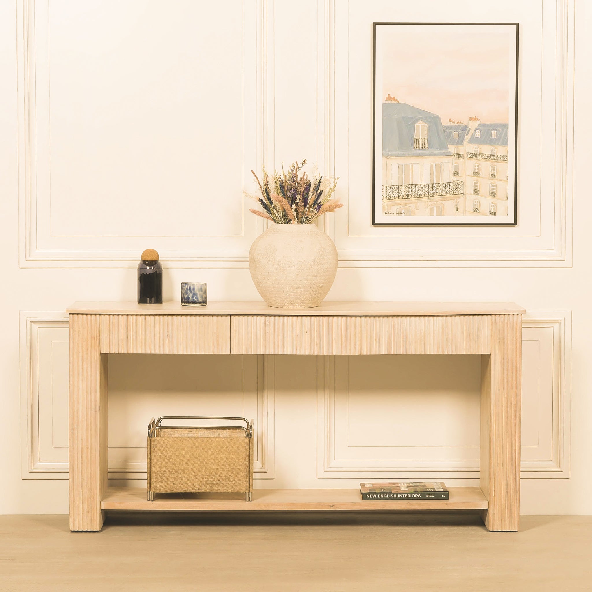 Camille fluted console table styled in a bright elegant hallway with artwork and decorative accessories, showing its three drawers, acacia wood construction and practical lower shelf.