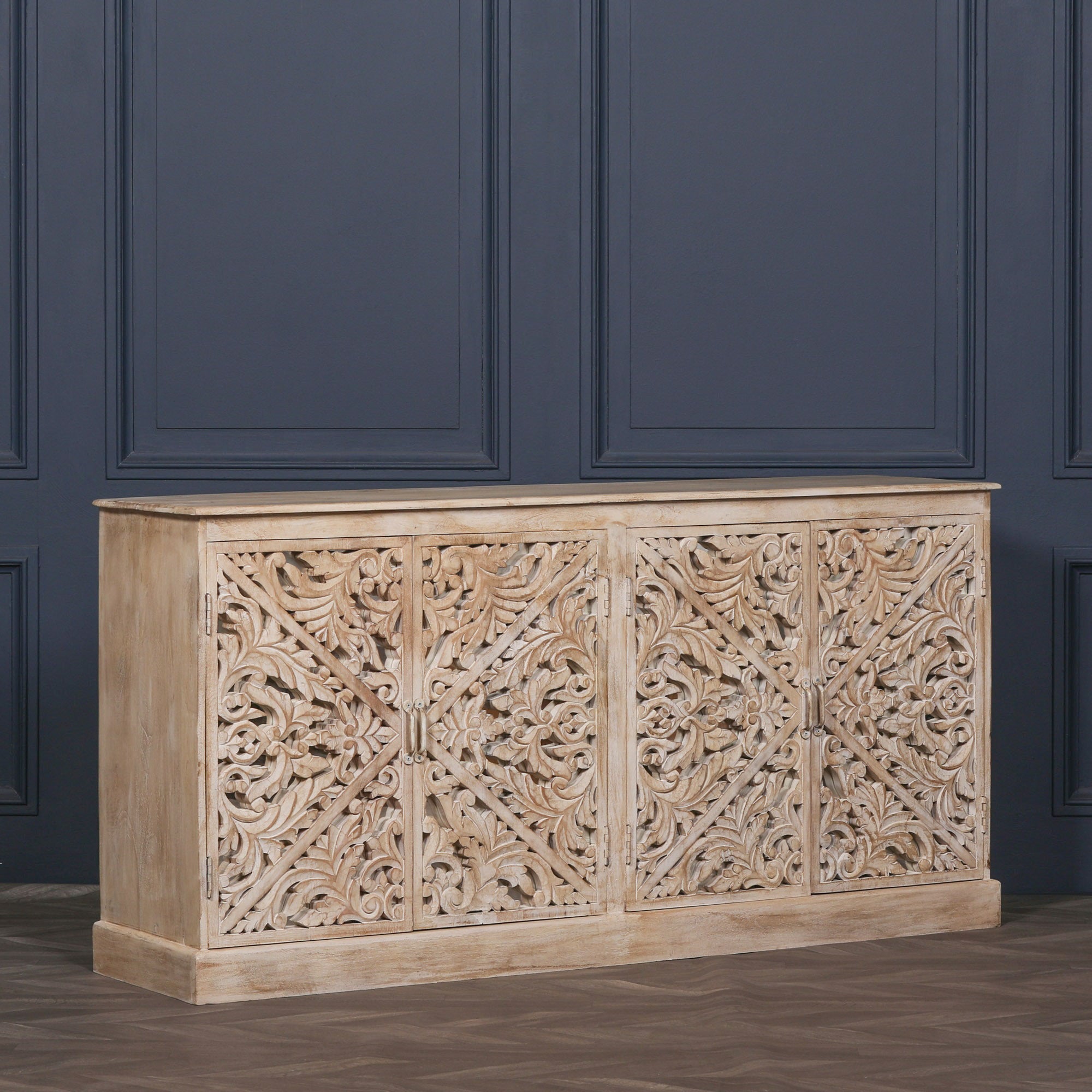 Angled view of the Camille Four Door Carved Mirrored Sideboard showcasing bleached mango wood, ornate hand carved mirrored panels and elegant storage for living rooms, dining rooms or hallways.